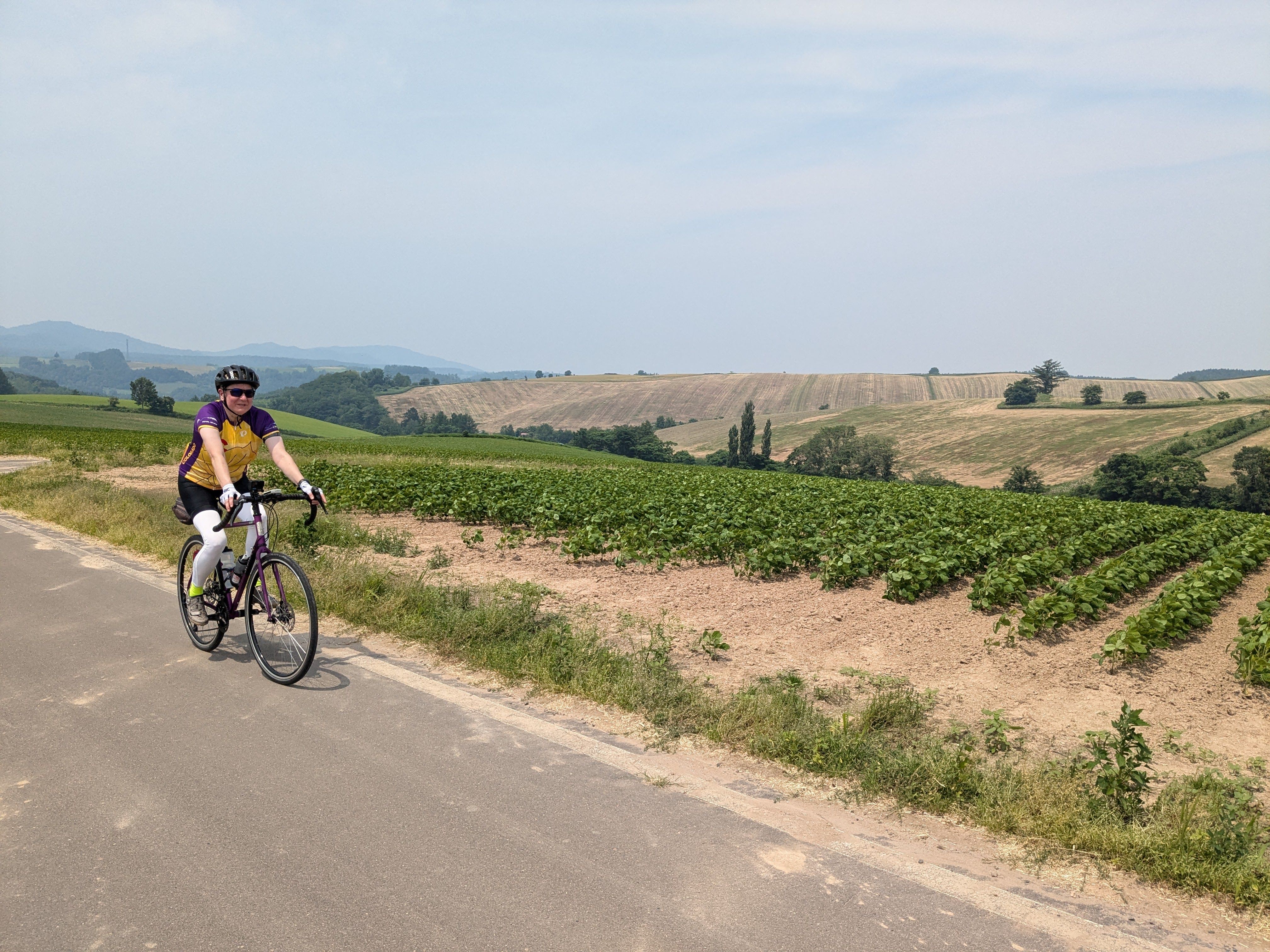 A cyclist smiles at the camera as she rides past the rolling hills of Biei, Hokkaido.