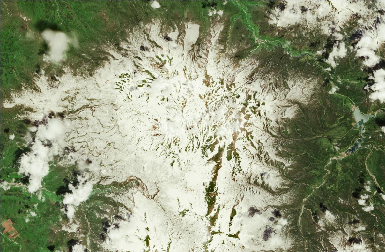A satellite image showing snow over the northern Daisetsuzan mountains. Strips of snow remain in the mountains while the rest of the landscape is green.