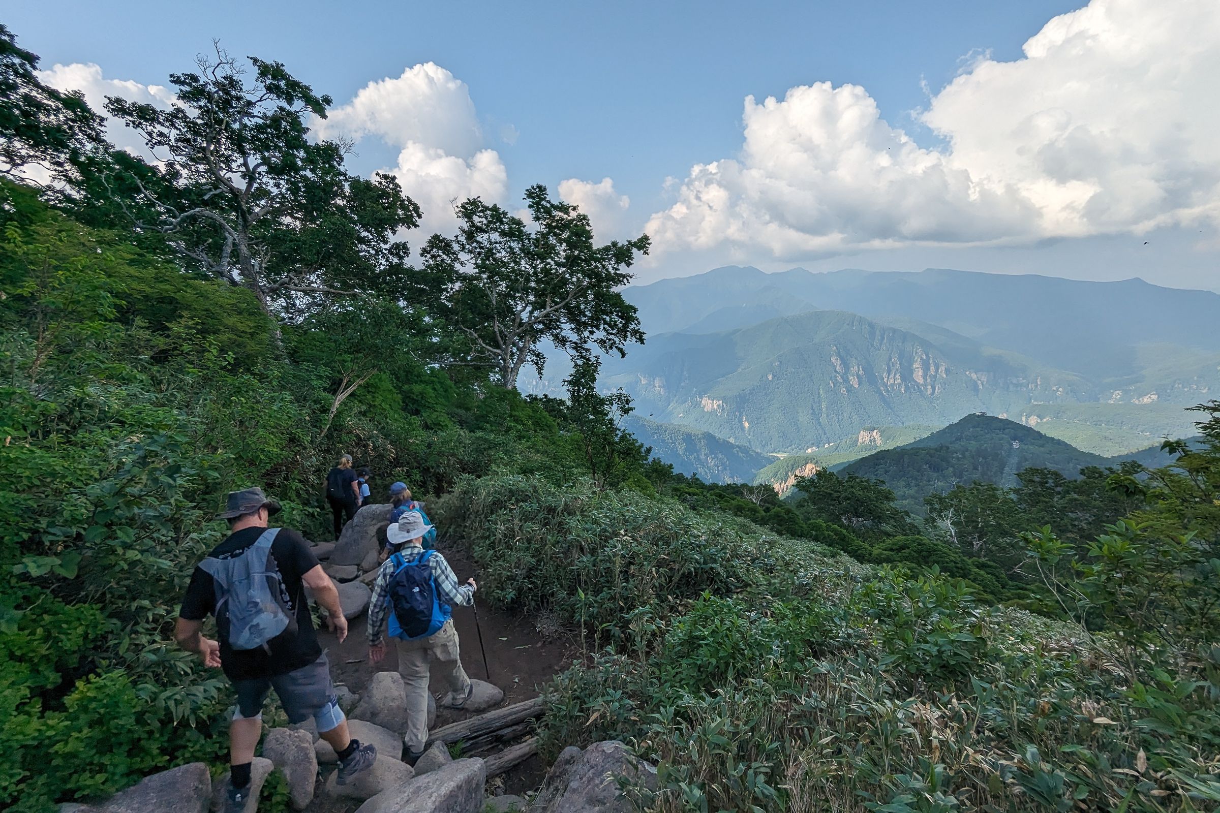 A group of hikers descent Mt Kurodake in the shade. Way below the walls of Sounkyo gorge can be seen catching the afternoon sun.