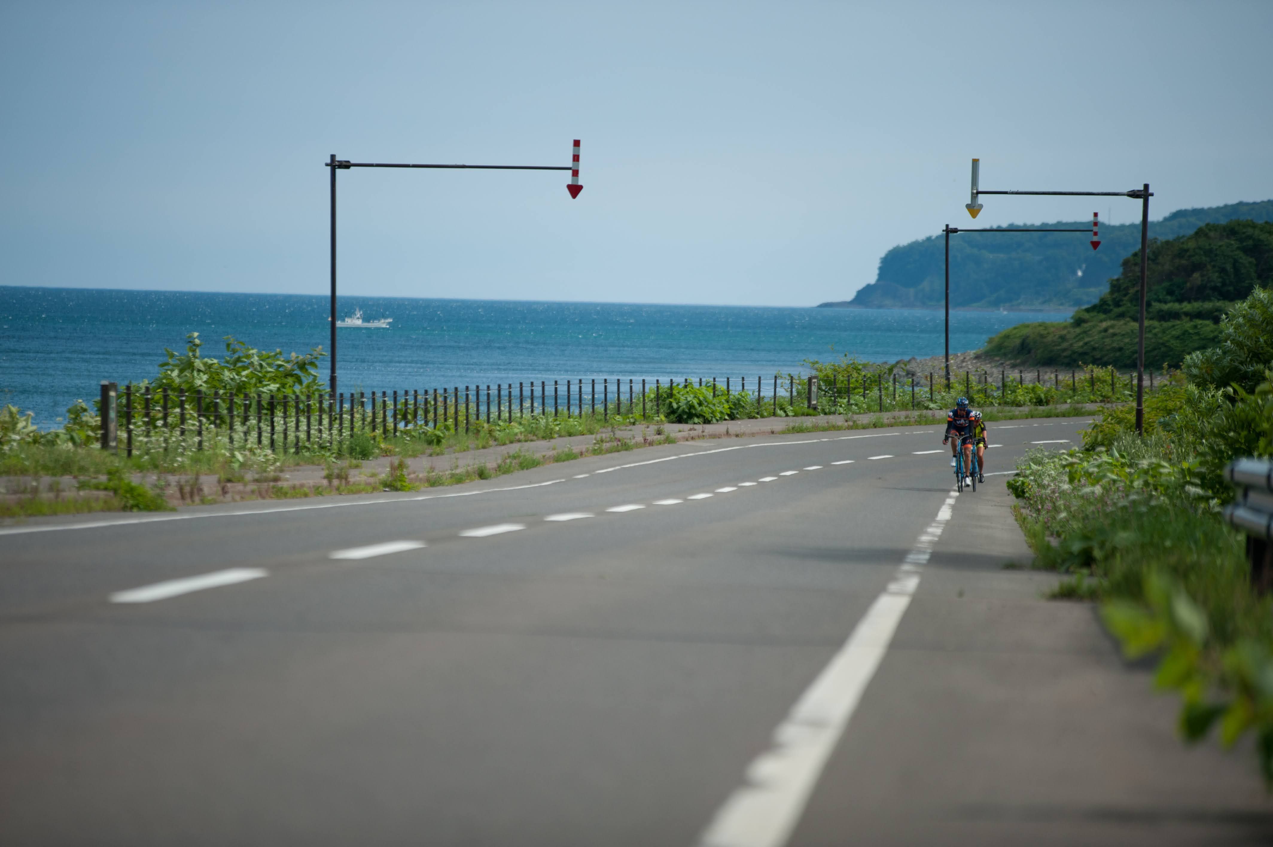 Two cyclists ride along the Sea of Okhotsk coast on a clear summer day.