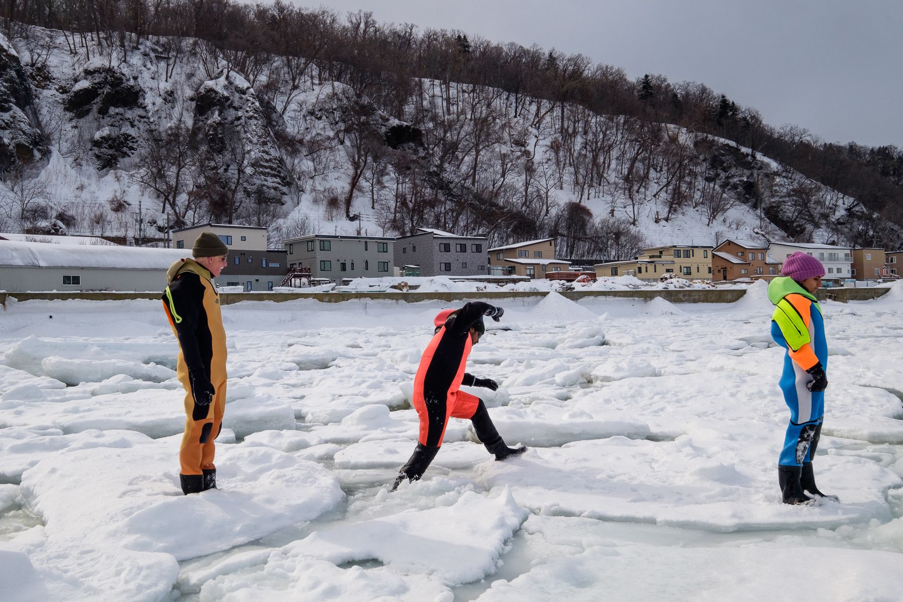 A tourist in a bright dry suit steps across broken drift ice off the coast of Utoro in the Shiretoko Peninsula.