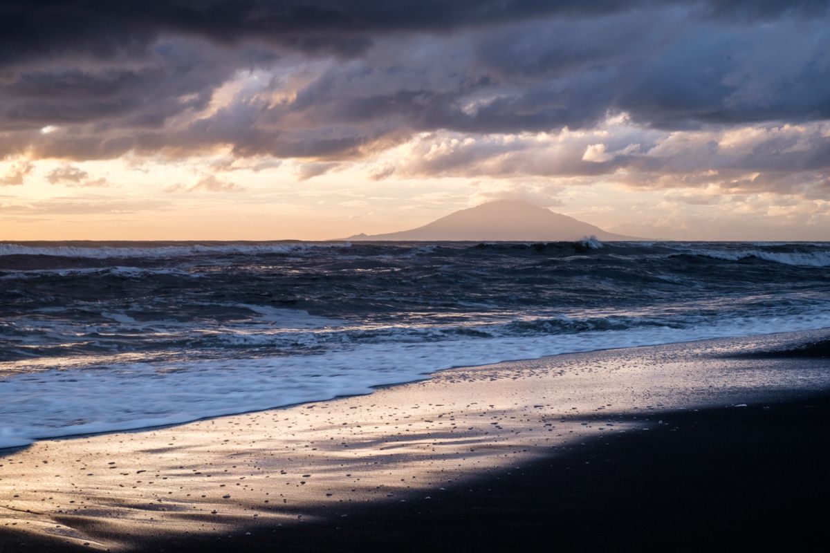 Mt Rishiri rising above the waves seen from a beach