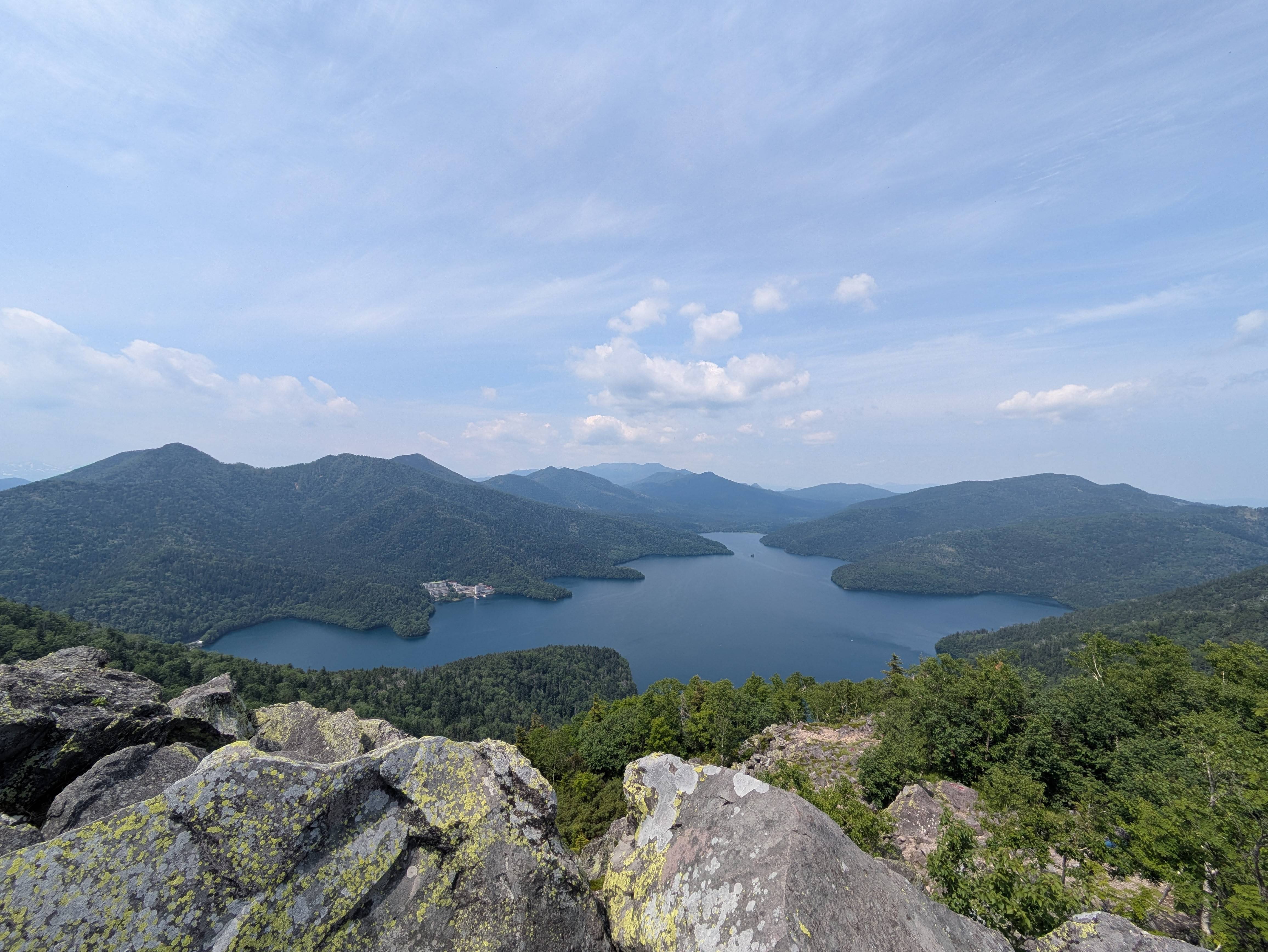 A beautiful view of Lake Shikaribetsu from the summit of Mt. Hakuundake, Hokkaido. It is a sunny day and the lake is perfectly reflecting the blue sky.