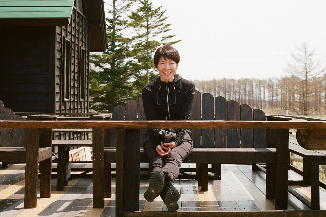 Adventure Hokkaido founder Ayaka smiles into the camera while she sits on a wooden bench located on an outside deck
