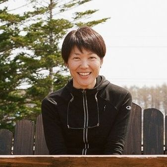 Adventure Hokkaido founder Ayaka smiles into the camera while she sits on a wooden bench located on an outside deck