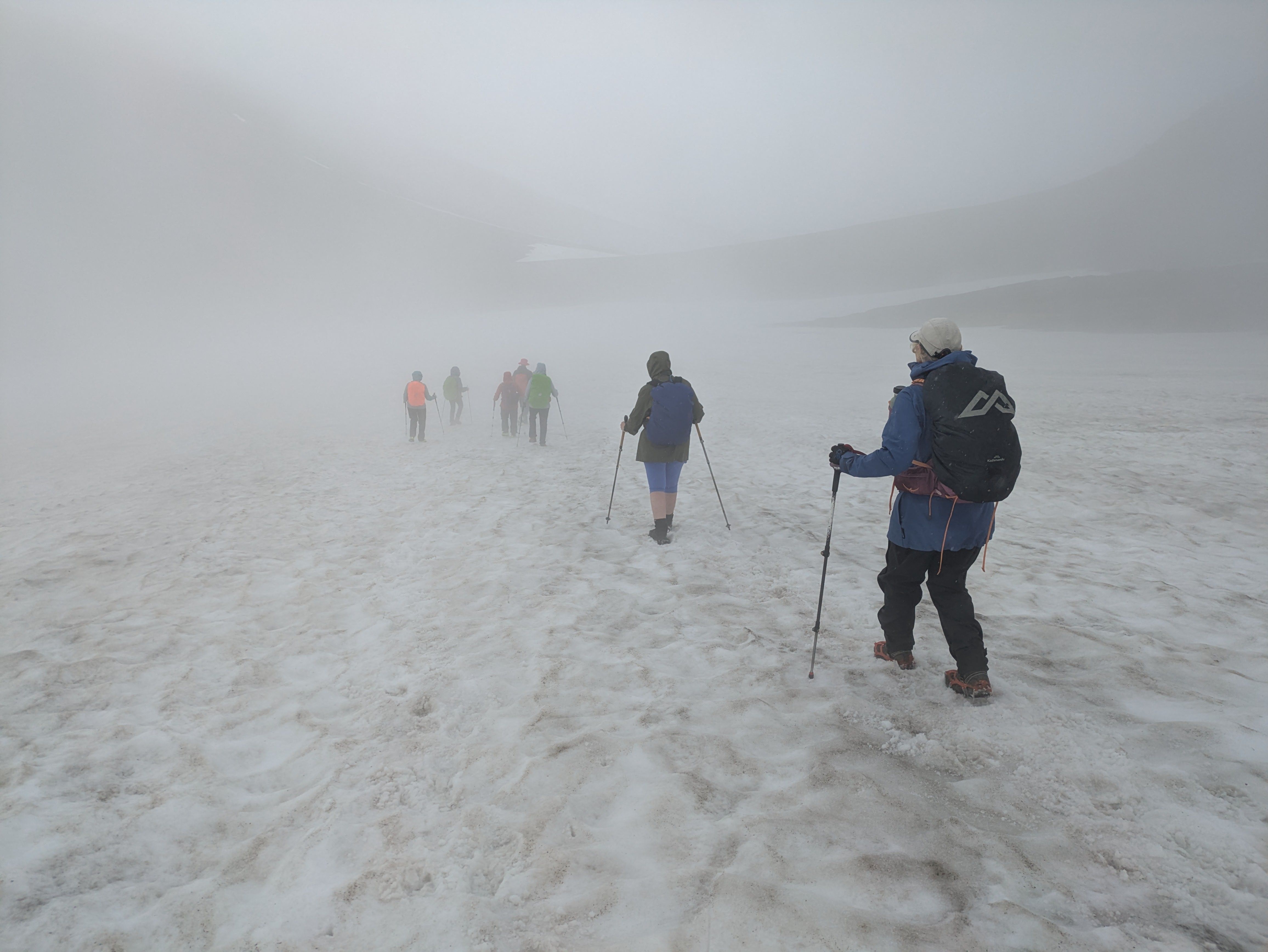 A group of hikers descend a snowfield in the mist in Daisetsuzan National Park. They are all dressed in warm clothes.
