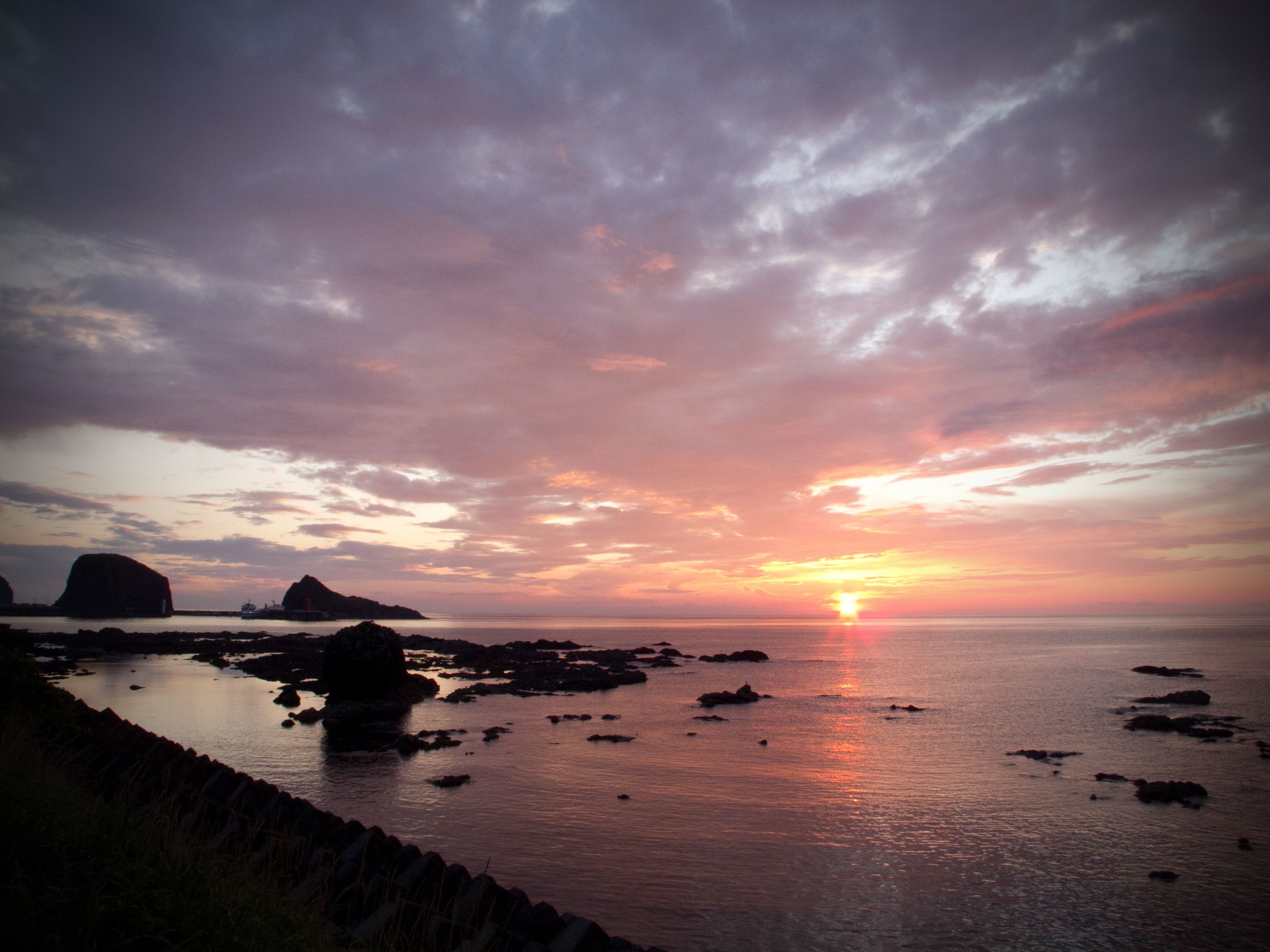 The setting sun casts diverse shades of pink, yellow and indigo across a flat, calm sea.