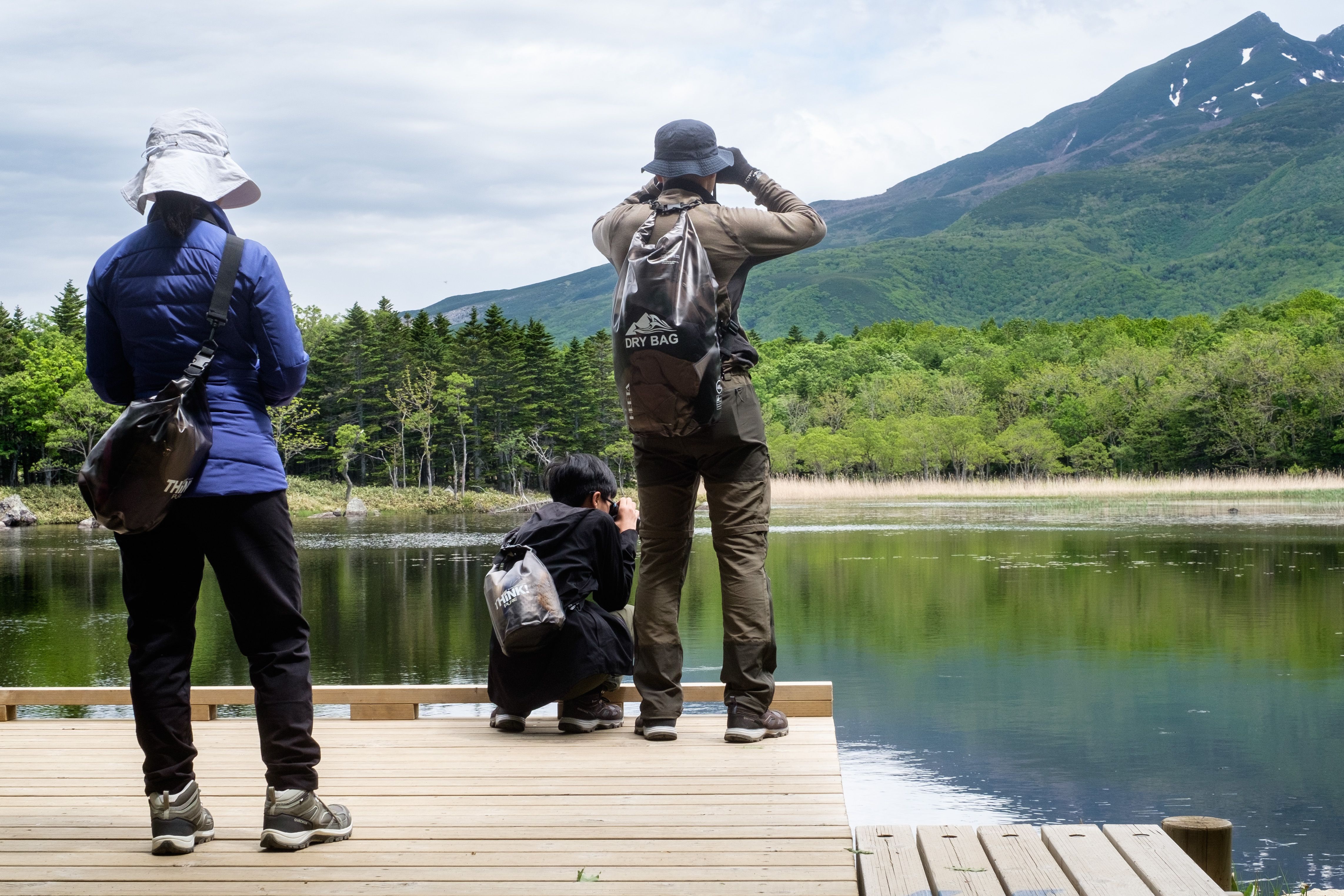 A family look for wildlife while standing on a deck next to a still lake.