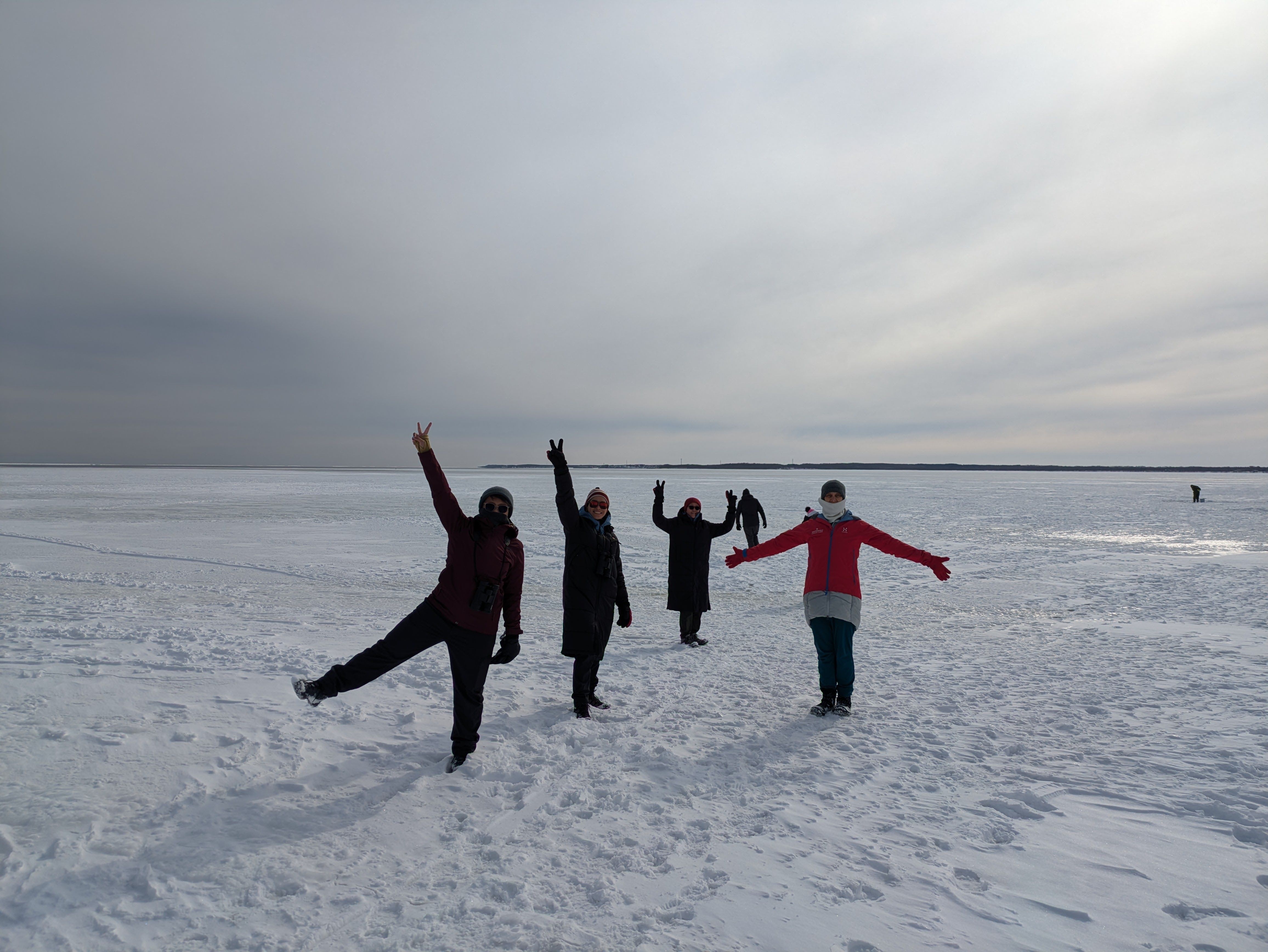 A group of people stand on a large ice field. The ice field stretches right out to the horizon.