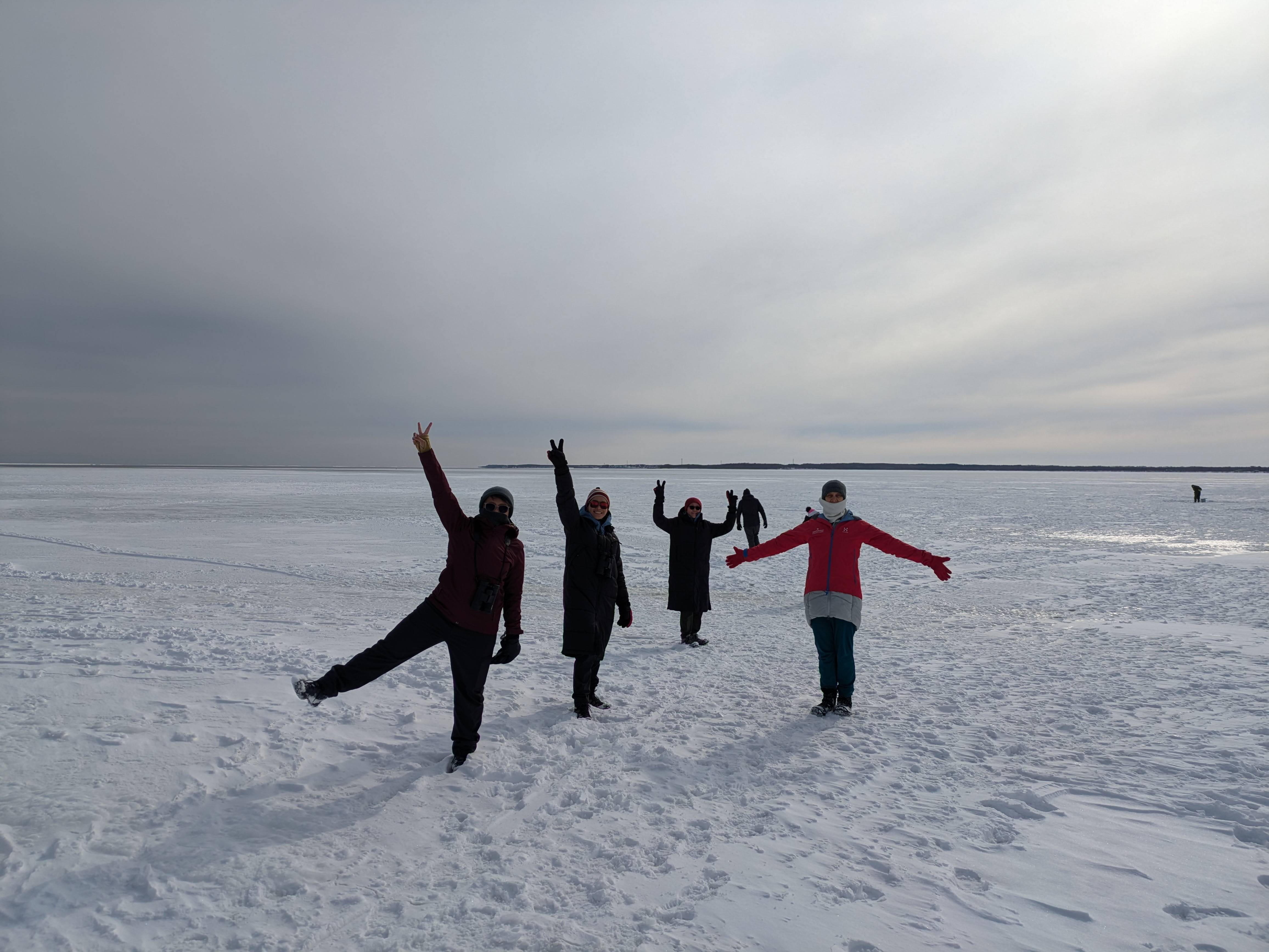 A group of people stand on a large ice field. The ice field stretches right out to the horizon.