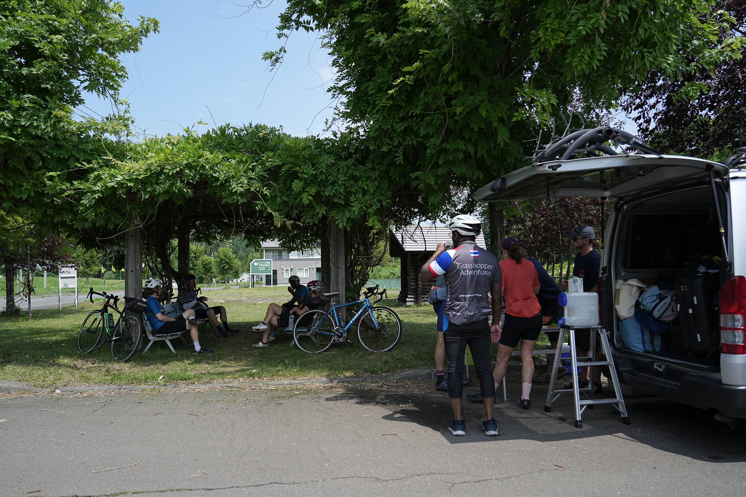 A group of cyclists taking a break at a picnic area on a summer day.