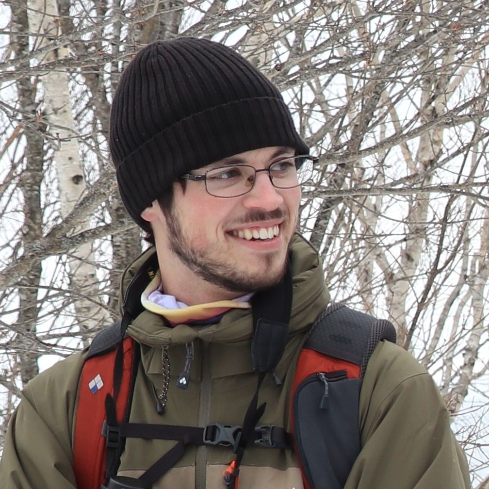 Adventure Hokkaido guide Zac stands in front of birch trees. It's winter and the trees have no leaves.