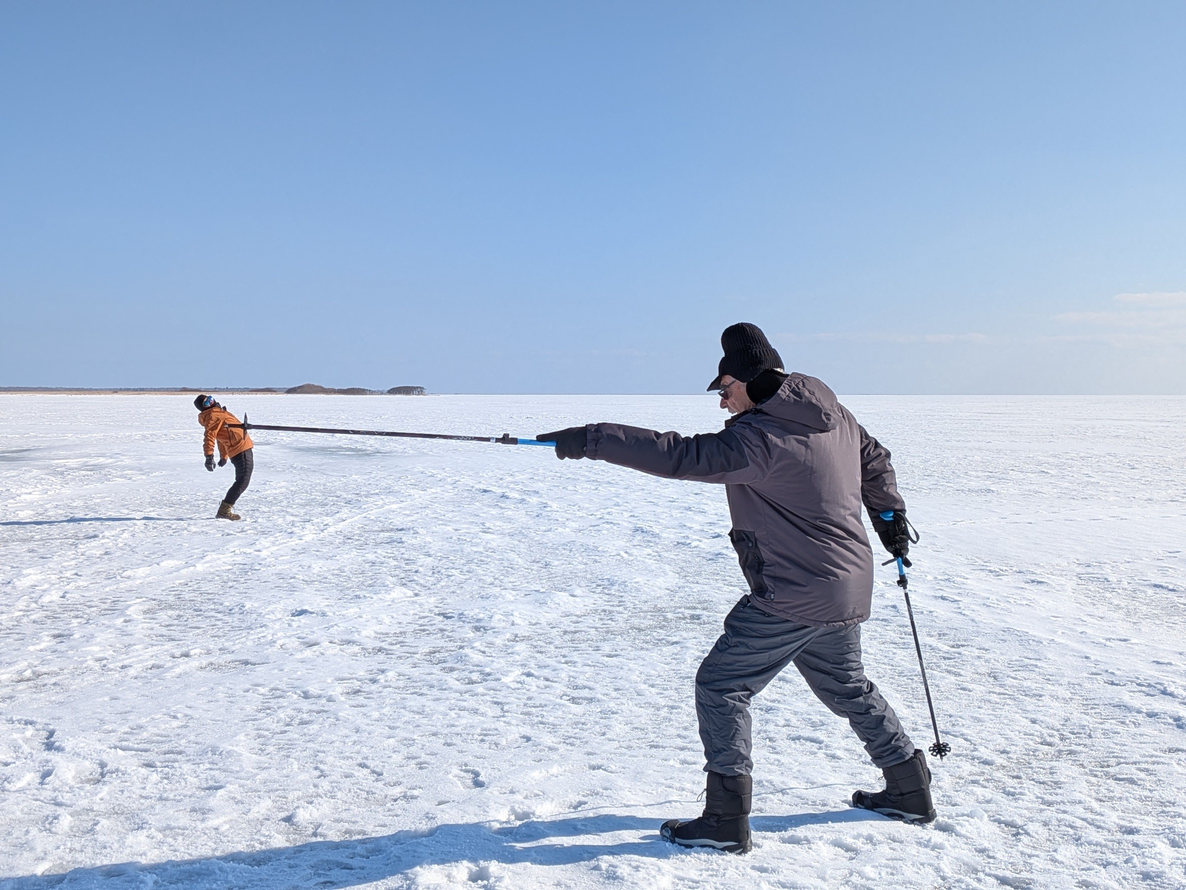 A man pretends to be spearing someone on the end of his snow pole. The person being speared is actually in the distance and the perspective of the vast ice field makes it appear as if they are very tiny and stuck on the end of his pole!