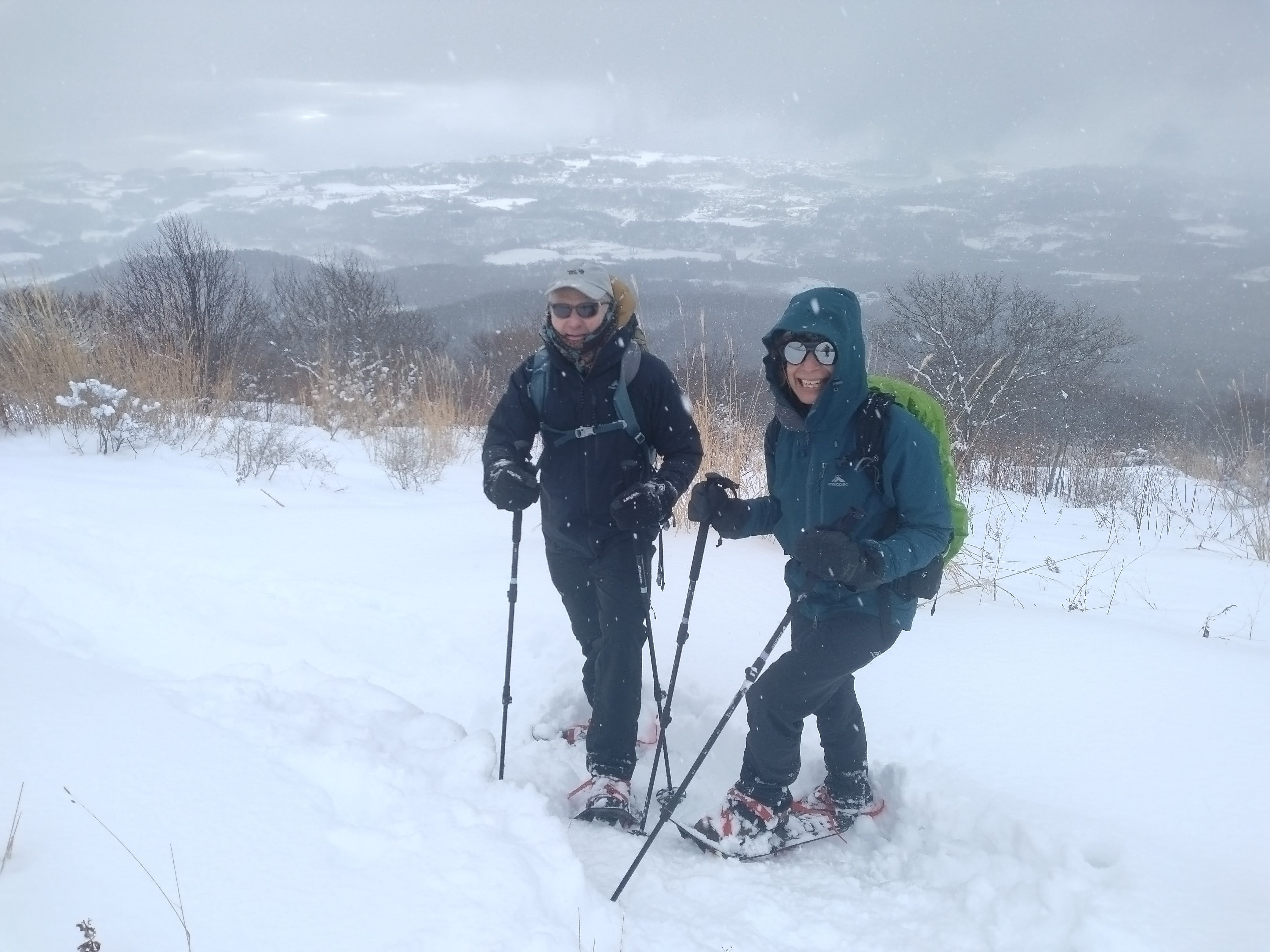 Two winter hikers in snowshoes smile at the summit of Mt. Usu. It is a snowy day.