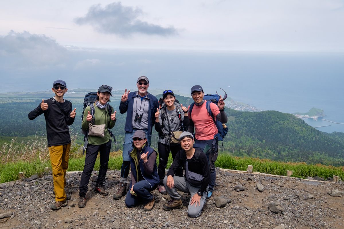 A group of hikers pose in front of sea views from Mt Rishiri