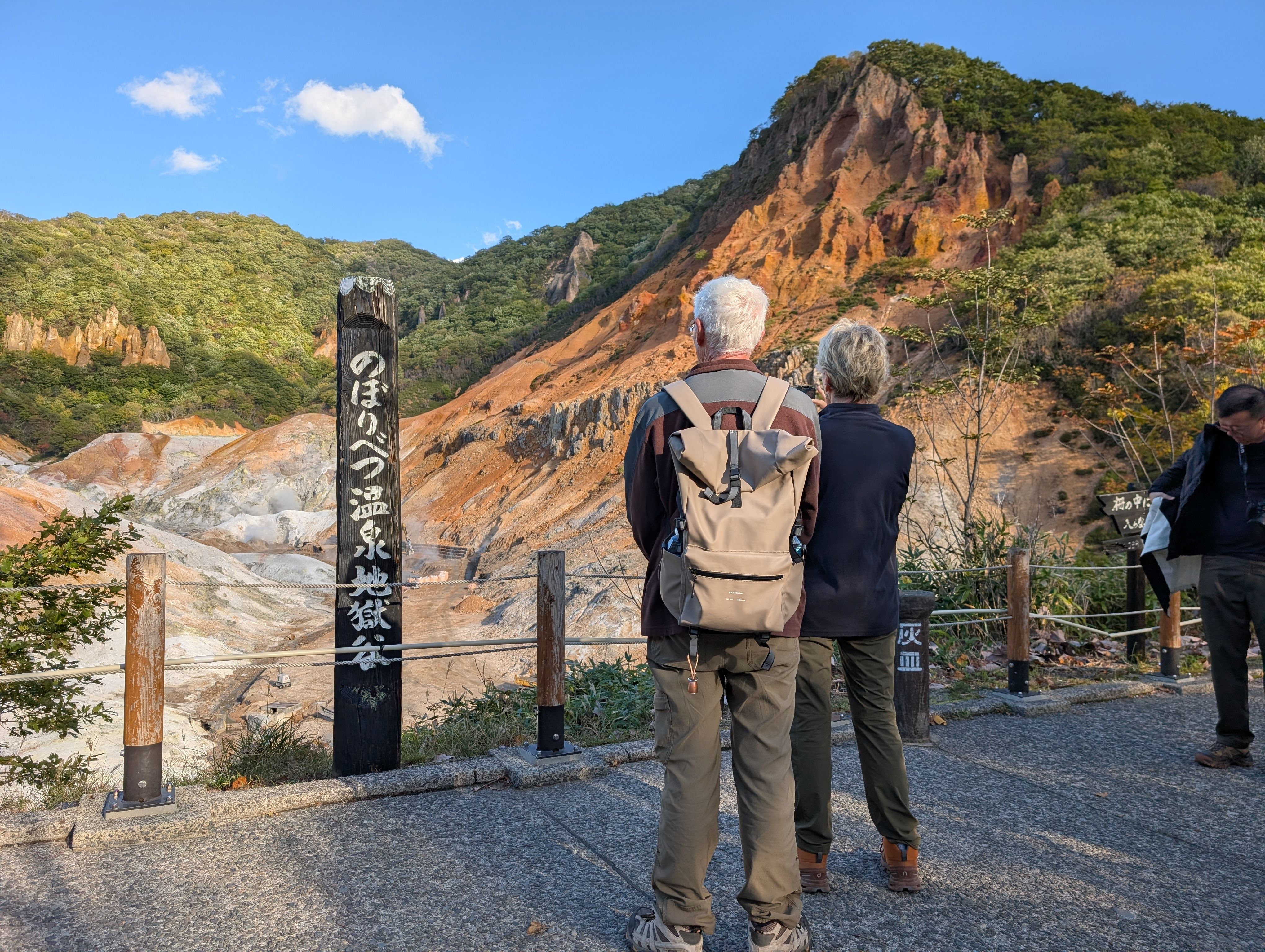 A couple look out at the volcanic valley in Noboribetsu. A sign in Japanese reads "Noboribetsu Onsen Hell Valley".
