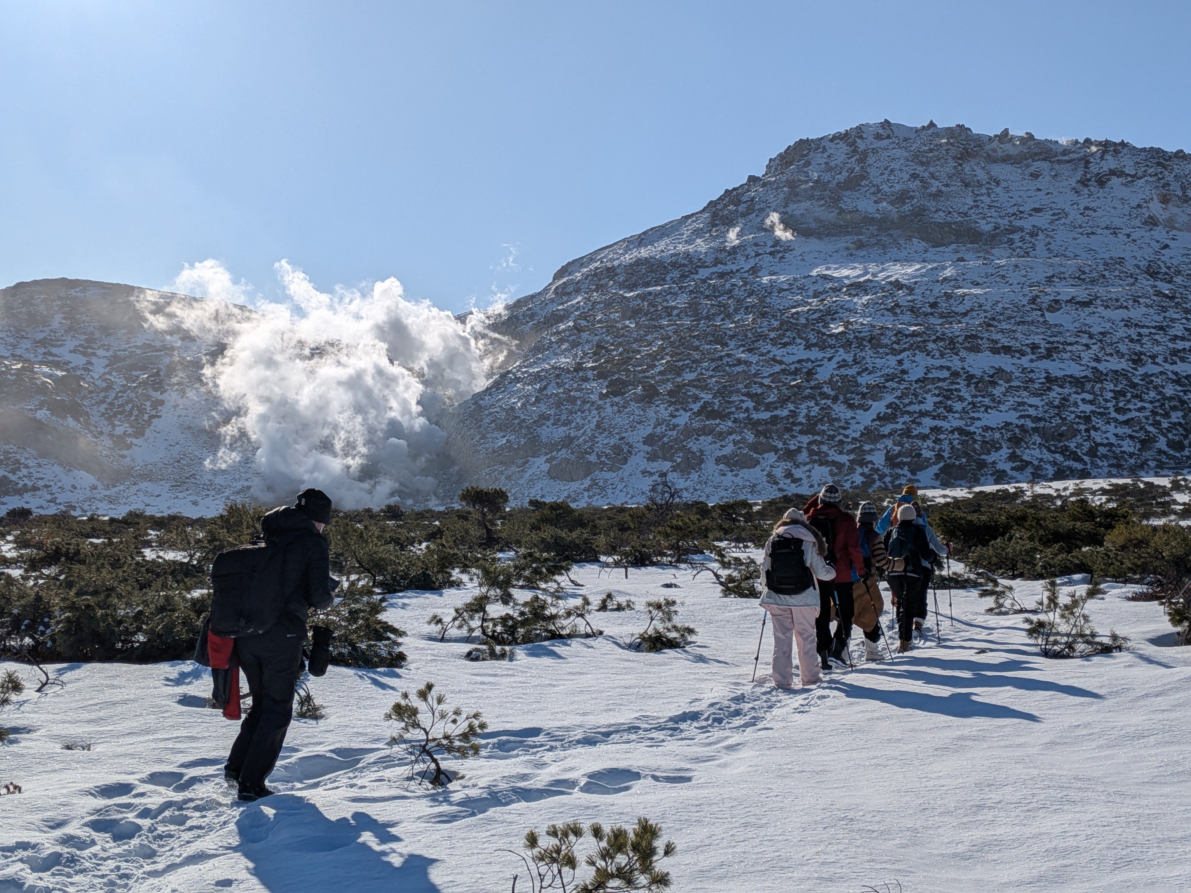 A group of walkers make their way through the snow towards Mt. Io in east Hokkaido. Steam is billowing from the volcanic crater between the two peaks.