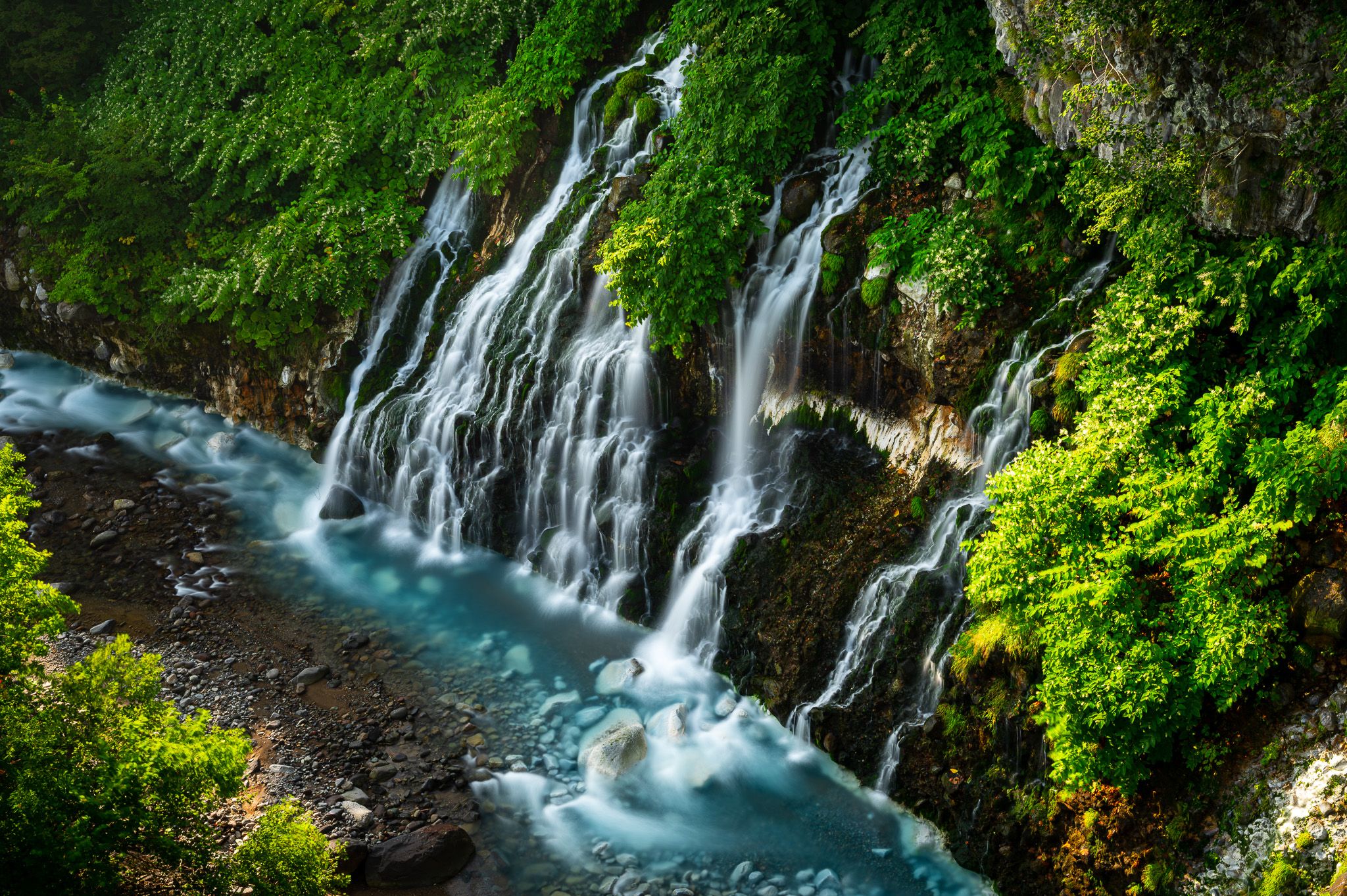 A slow-shutter shot of Shirahige Waterfall in Shirogane Onsen. The slow shutter time makes it look as if the streams of the waterfall are mist.