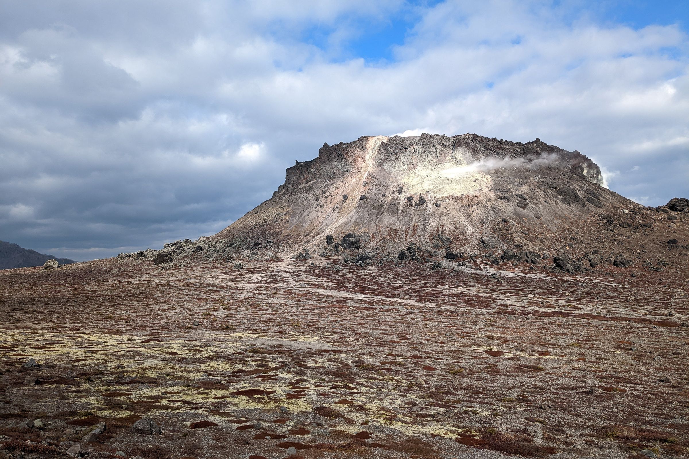 The barren lava dome of Mount Tarumae, characterised by its distinctive flat top and active fumaroles, features a rugged volcanic landscape with minimal vegetation and exposed rocky terrain.