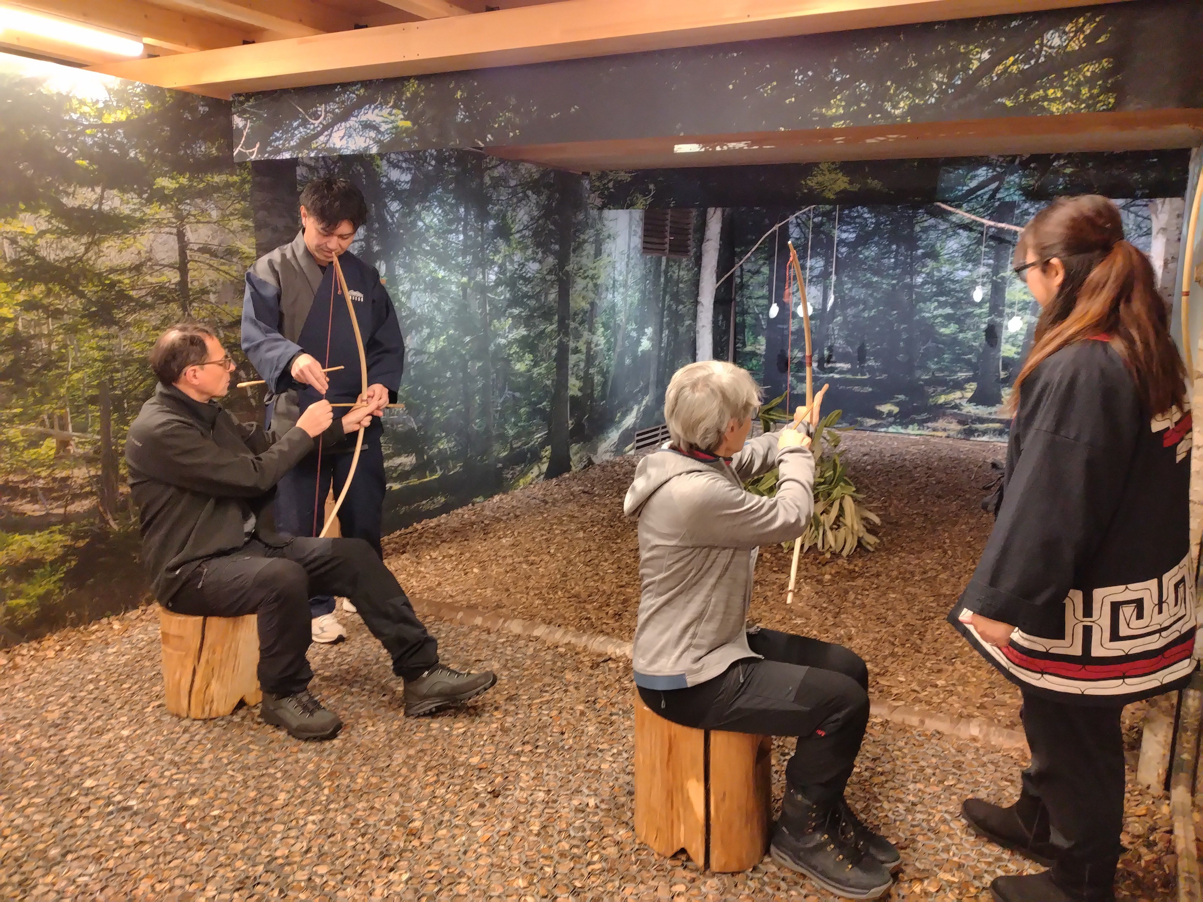 Two guests try their hand at traditional Ainu archery at Upopoy National Ainu Museum in Hokkaido. Two members of museum staff supervise and help them with their technique.