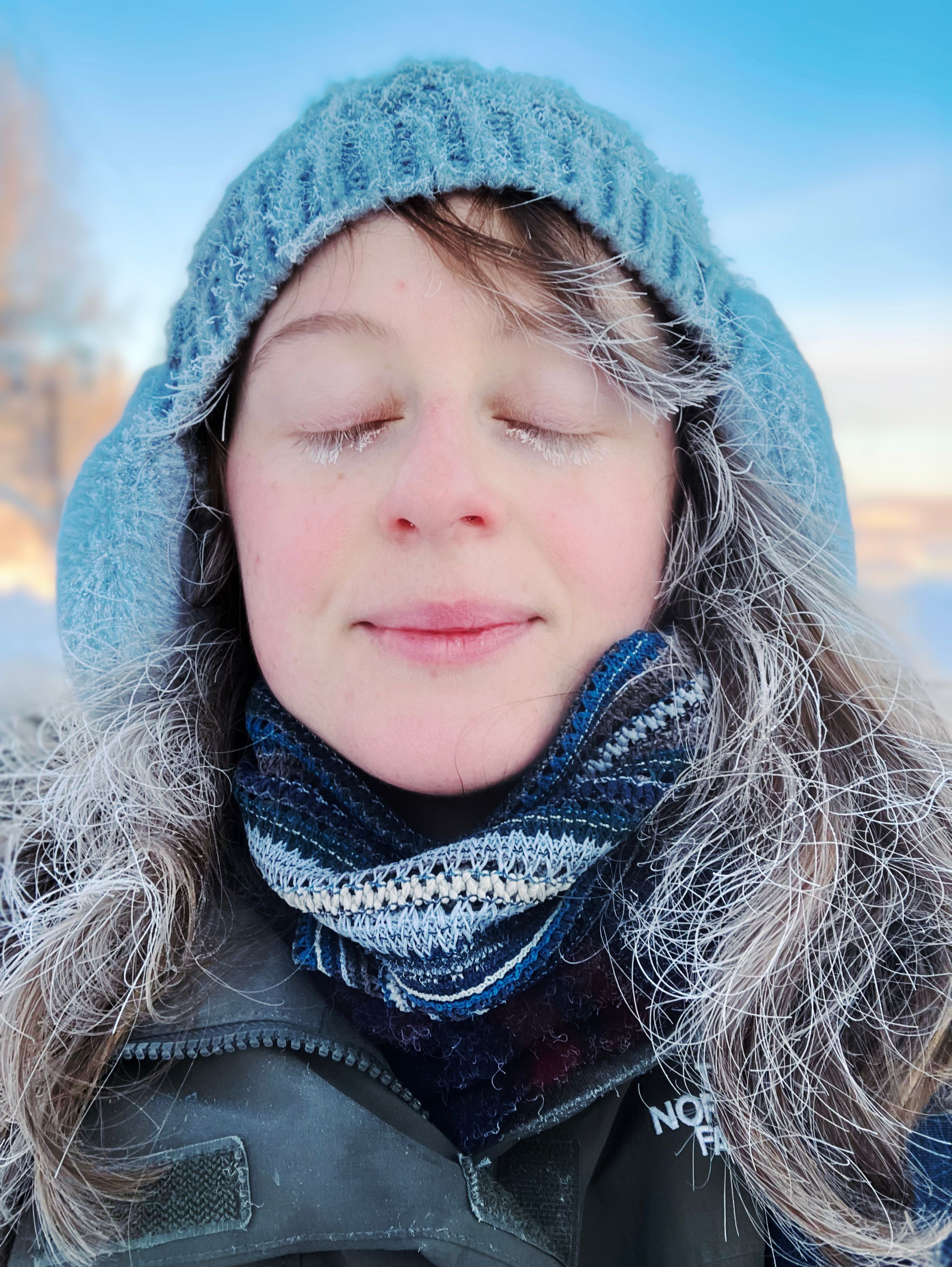 A girl closes her eyes in the cold, her eyelashes and hair frozen solid.