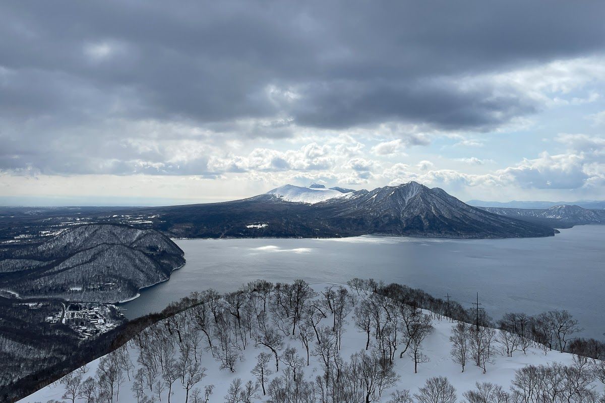 A lake stretches away from below a precipice, with a mountain rising out of the lake in the background.