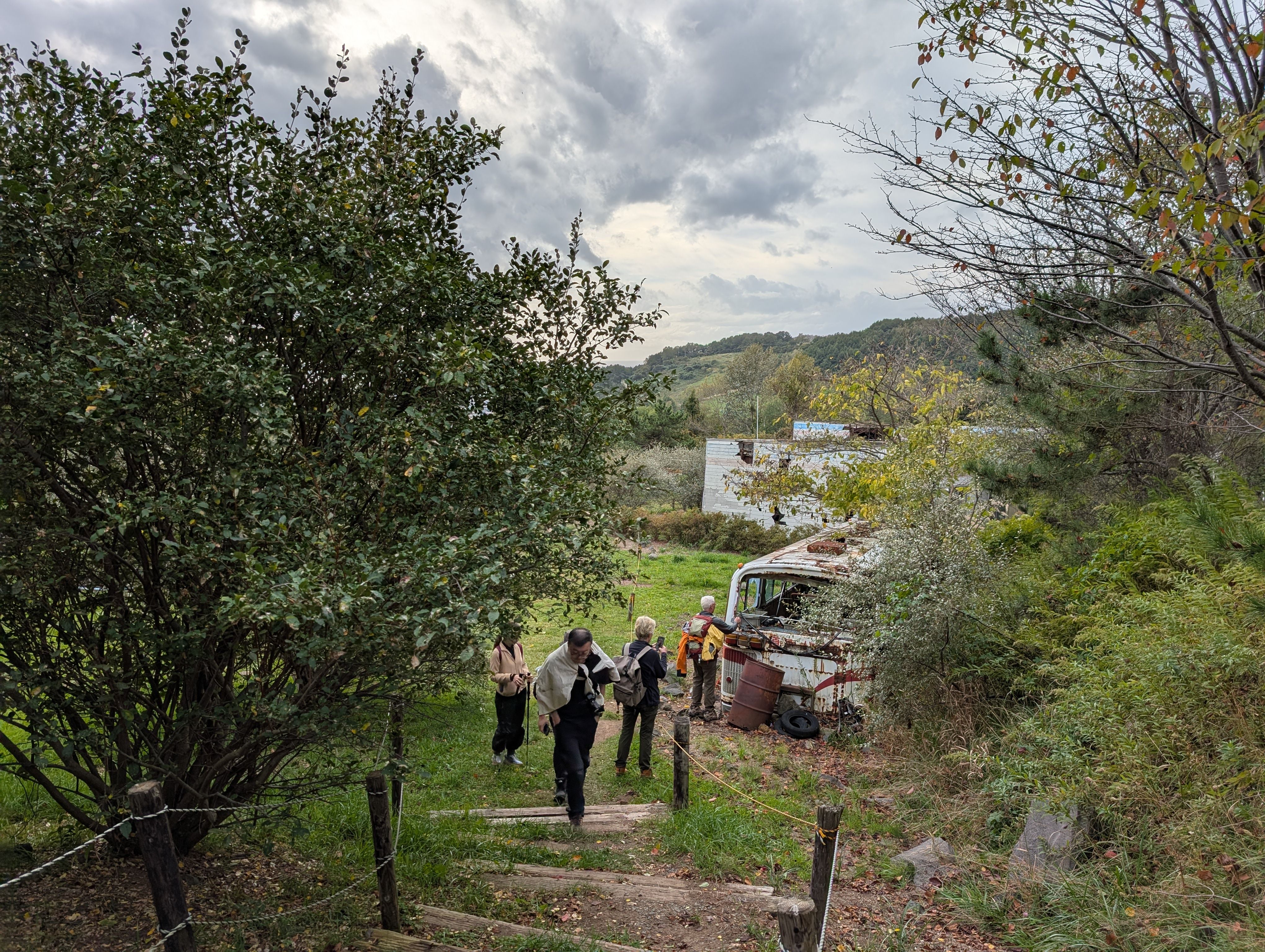 A group of hikers survey the damage done to a kindergarten and school bus by a 2000 volcanic eruption. The building and the bus are covered in holes where rocks from the eruption ripped through them.