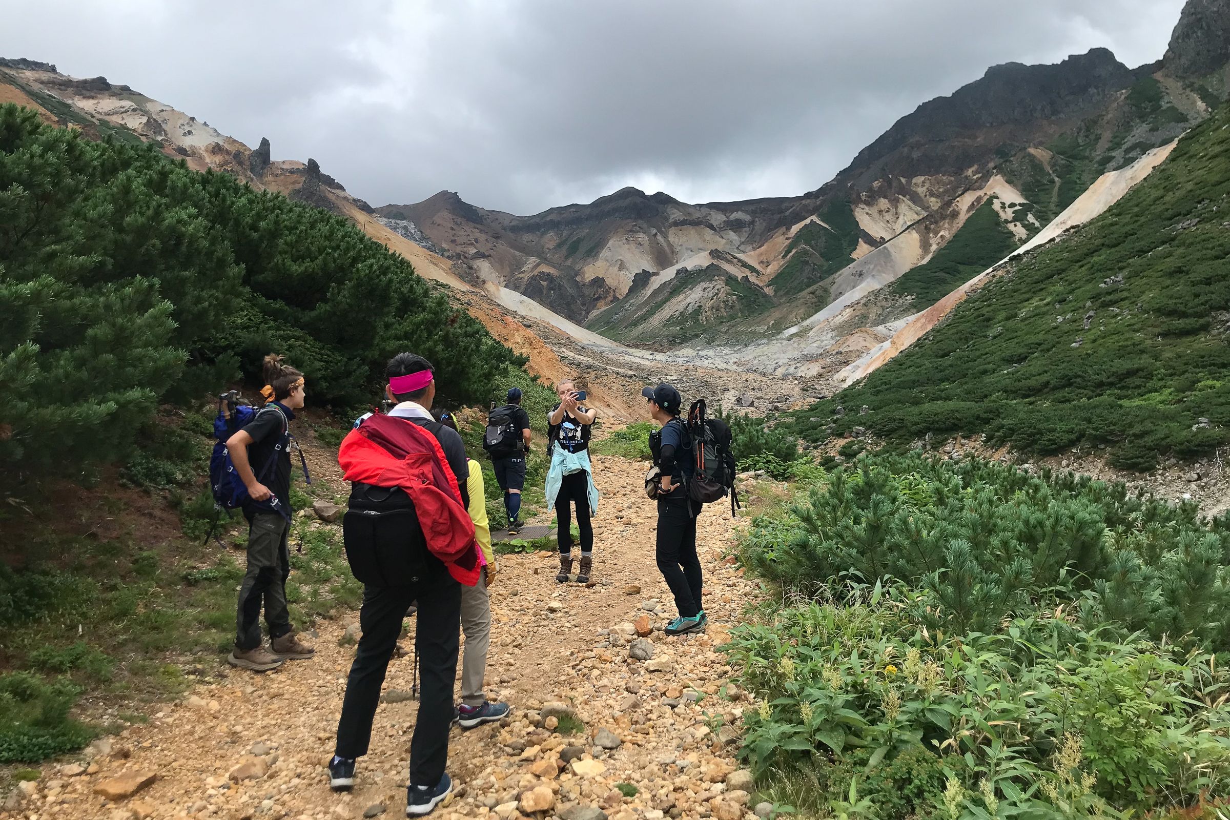 A group of hikers pose for photos on a rocky hiking route heading into a volcanic crater.