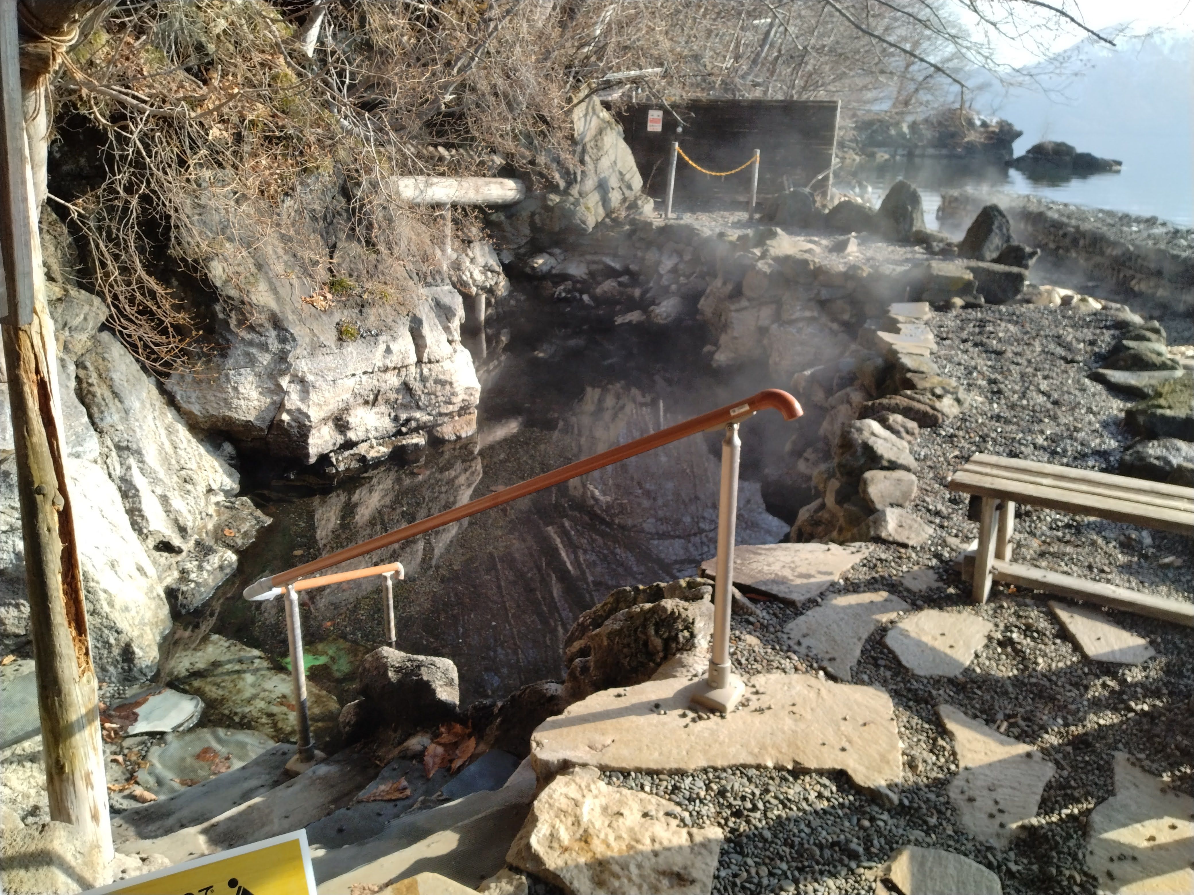 A rocky outdoor bath beside Lake Shikotsu steams in the morning light.