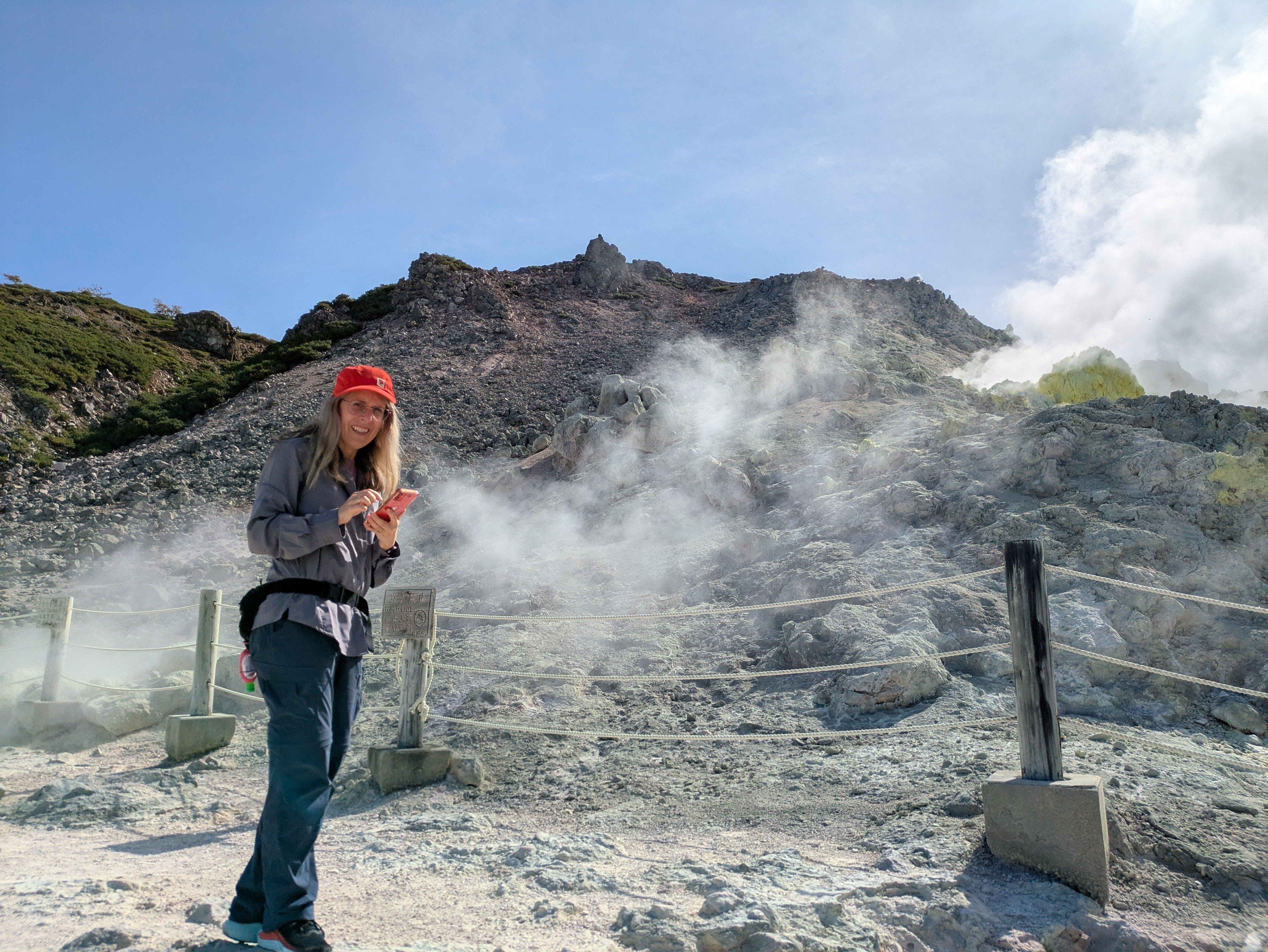 A woman smiles at the camera in front of volcanic vents on Mt. Io, Hokkaido.