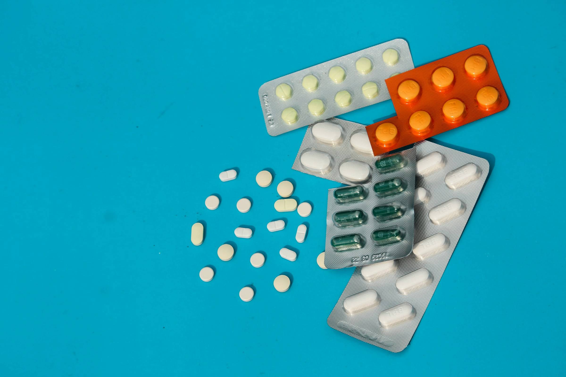 An assortment of medications for traveling, including several blister packs and loose pills of various colors, scattered on a bright blue surface.
