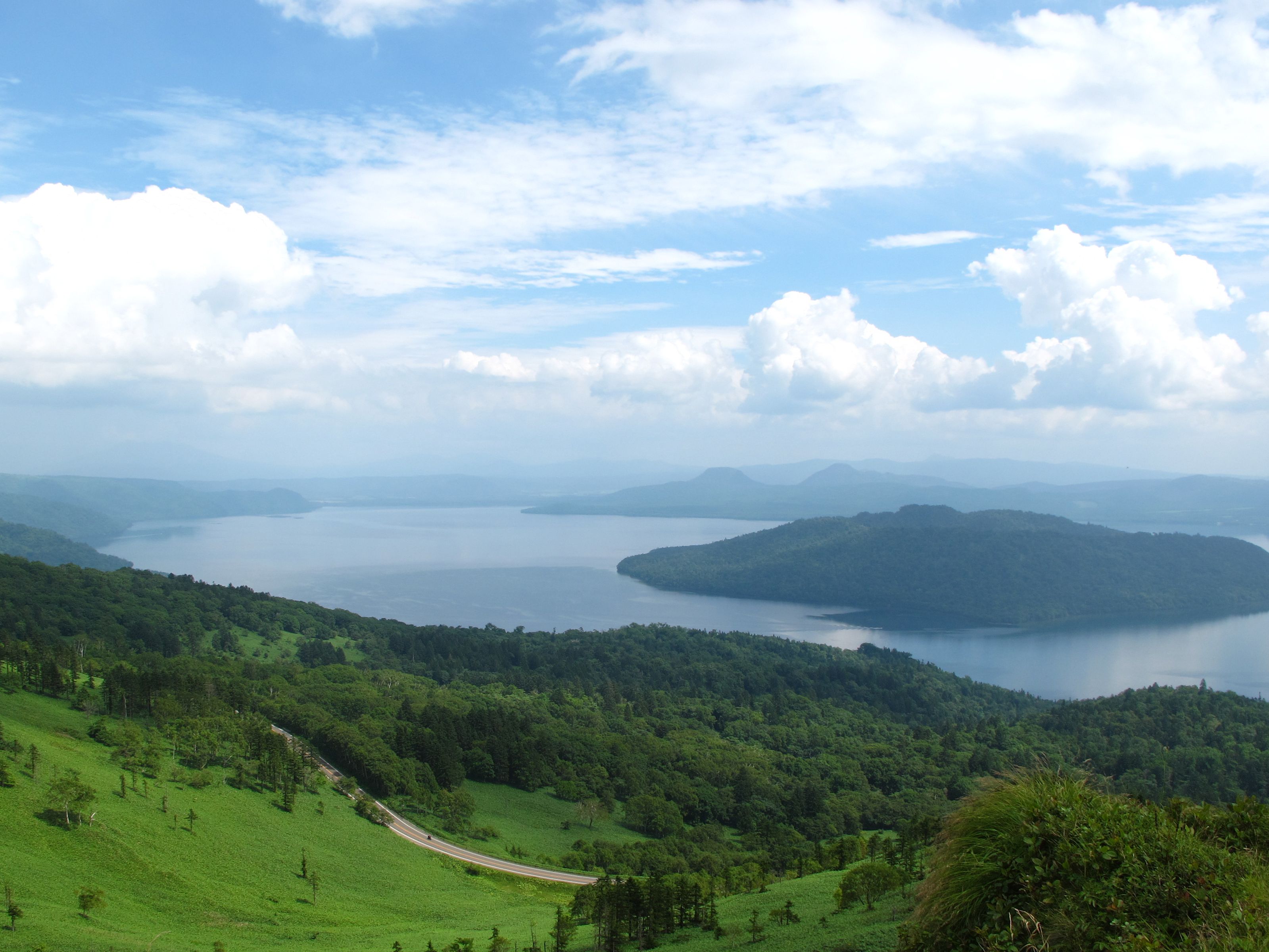 A view of Lake Kussharo with blue skies and fluffy white clouds.