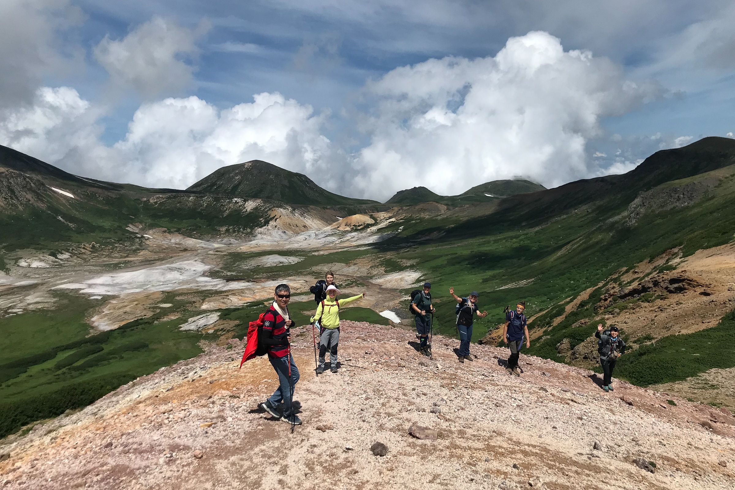 Seven hikers in Daisetsuzan National Park wave to the camera on a sunny day.