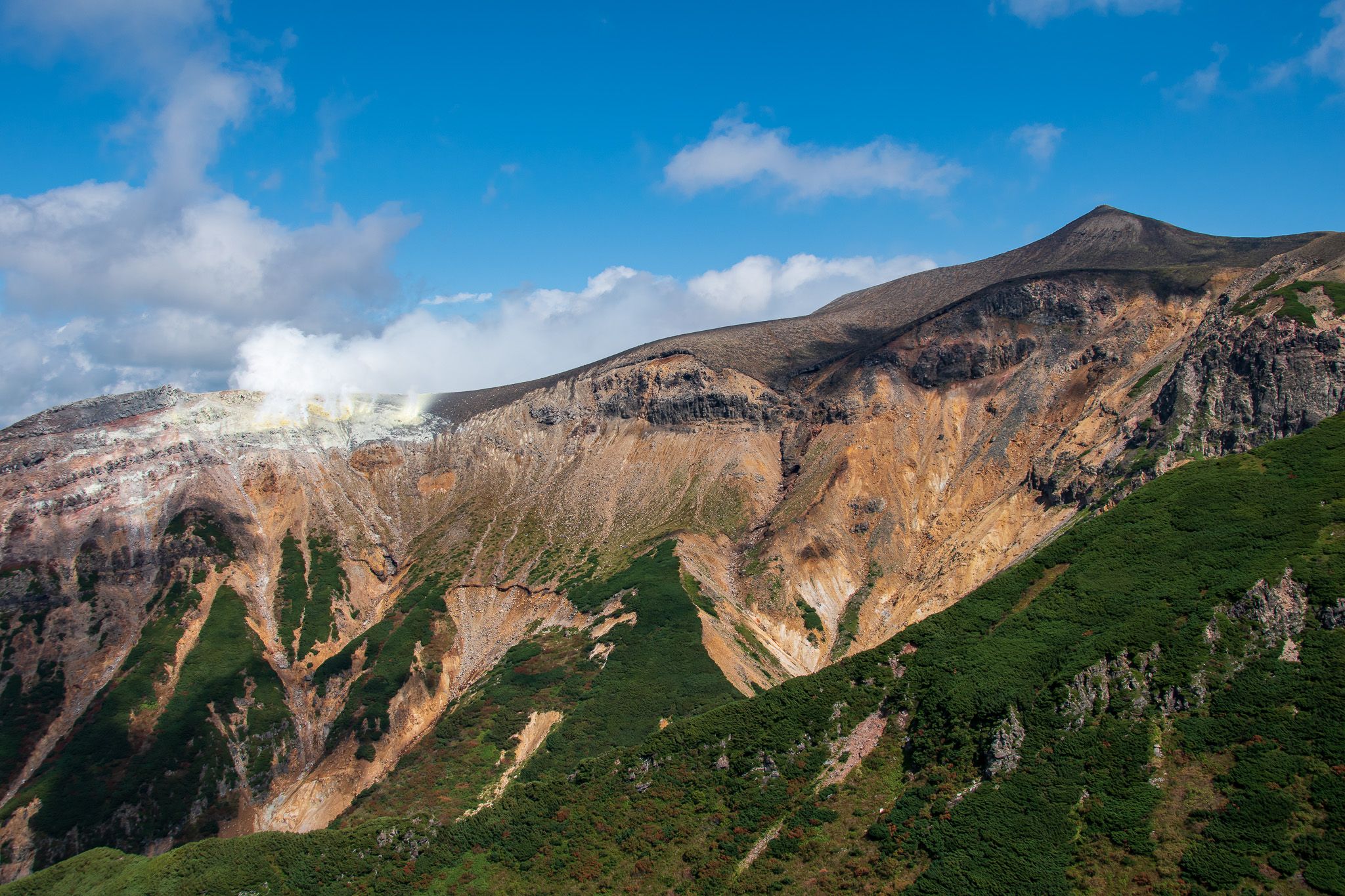 The rocky south face of Mt. Tokachi as viewed from Mt. Sandan, The summit is seen on the right and steam is rising from vents on Mae-tokachi on the left.