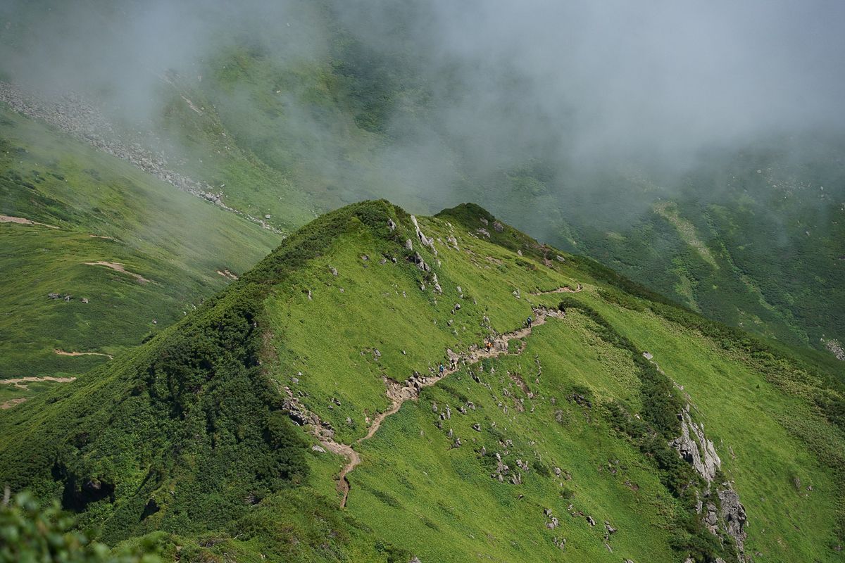A group of hikers seen in the distance dwarfed by the scale of the Daisetuzan Mountains