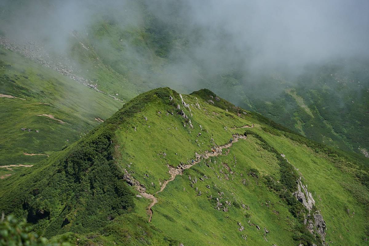 A group of hikers seen in the distance dwarfed by the scale of the Daisetuzan Mountains