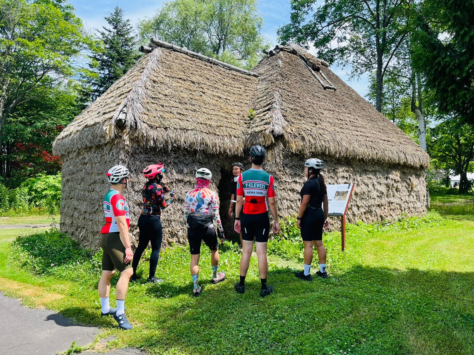 A group of cyclists stand outside an Ainu cise in Asahikawa, Hokkaido. A cise is a traditional Ainu dwelling made from timber and bamboo grass.