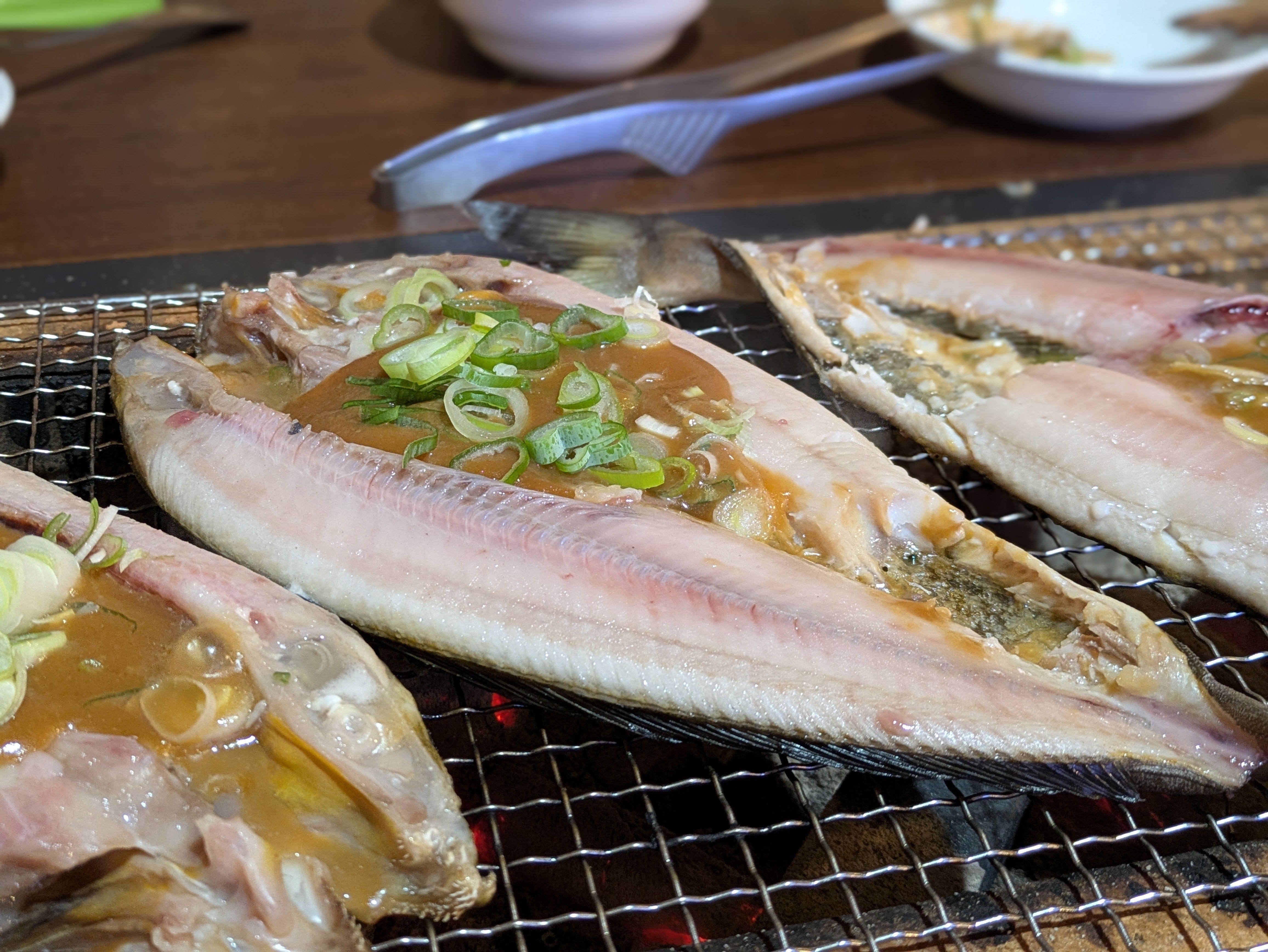 A photograph of Atka mackerel on a grill, a fish that is characteristic of Hokkaido cuisine. The fish has been butterflied and filled with miso and spring onions, ready to grill.