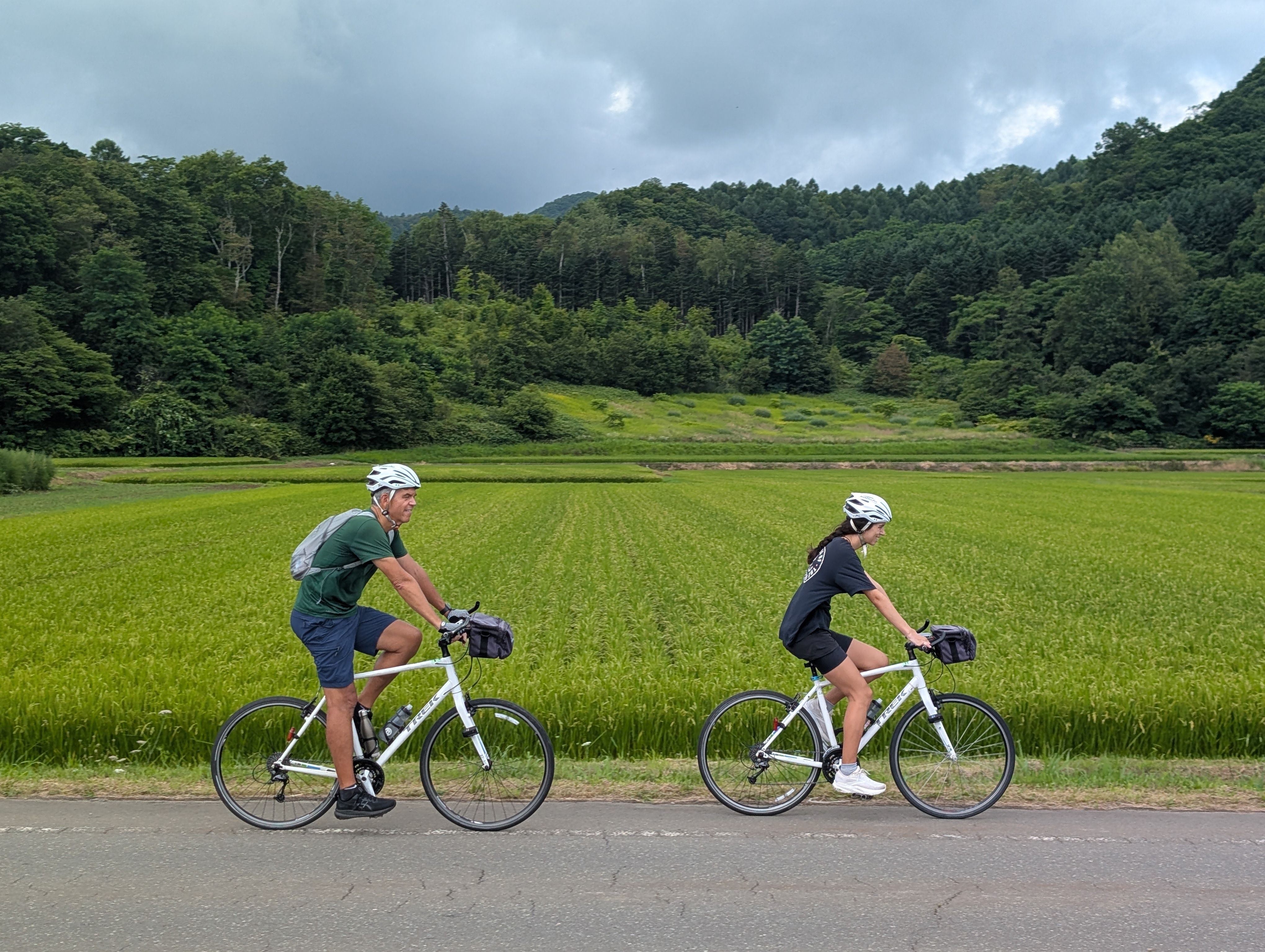 Two cyclists ride past a large rice paddy.