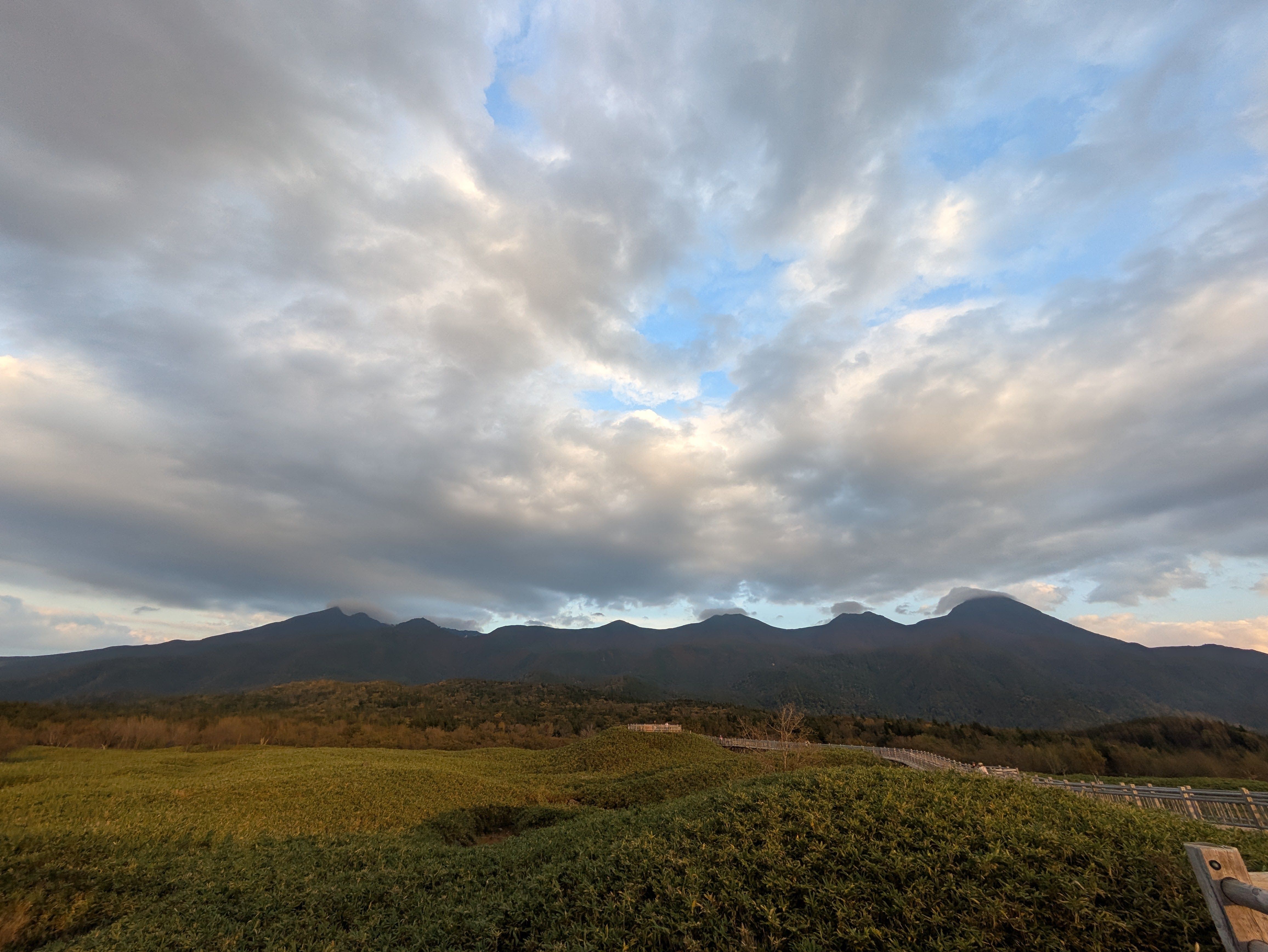 A wide angle shot of the Shiretoko mountains visible from Lake Five of the Shiretoko Five Lakes. It is late afternoon and the sky is growing dark and the light is a little golden.