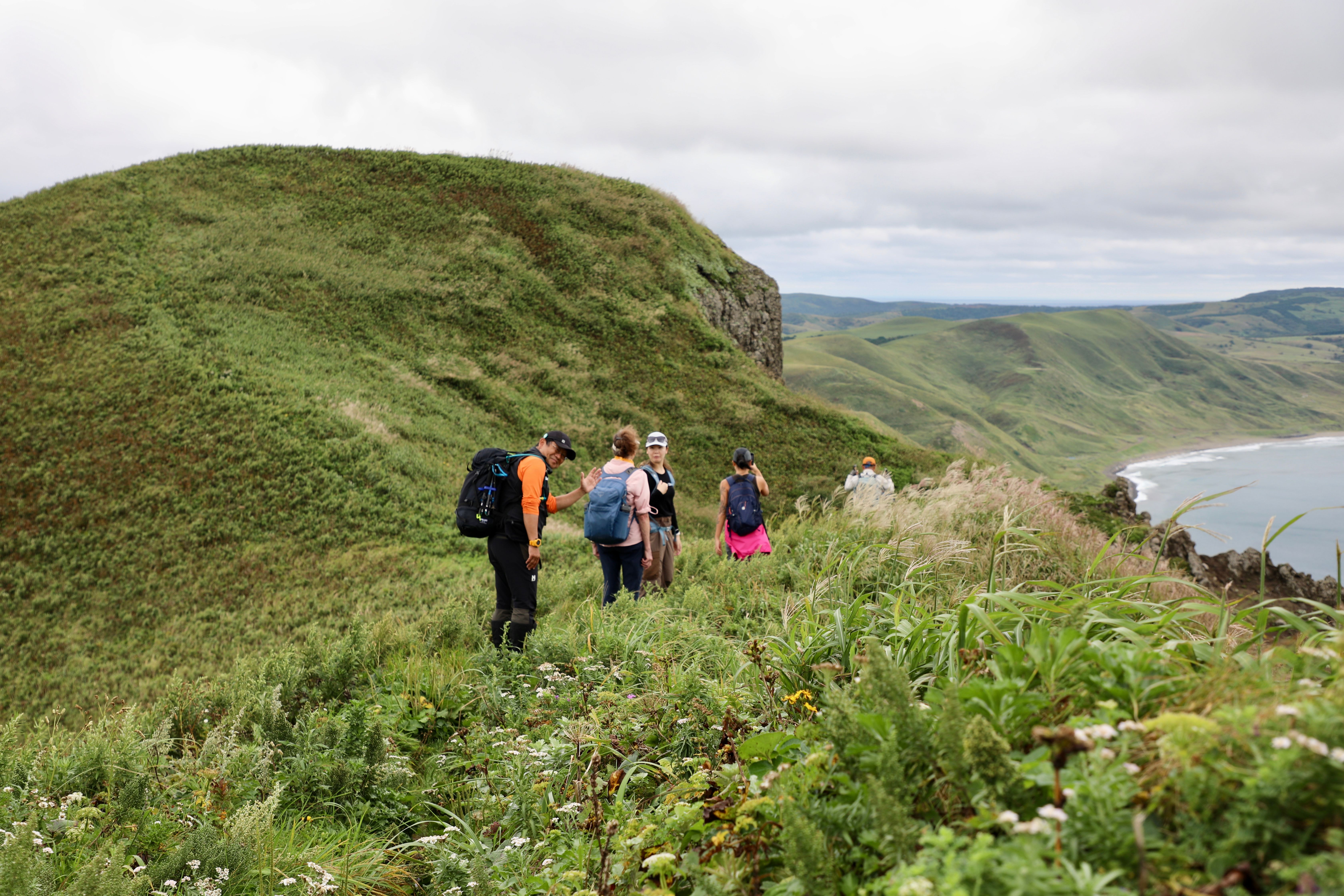 A group of hikers walks through grassland on a hiking route on Rebun Island. The individual at the back of the line is turning back to wave at the camera. (Photo by Samir Patel)