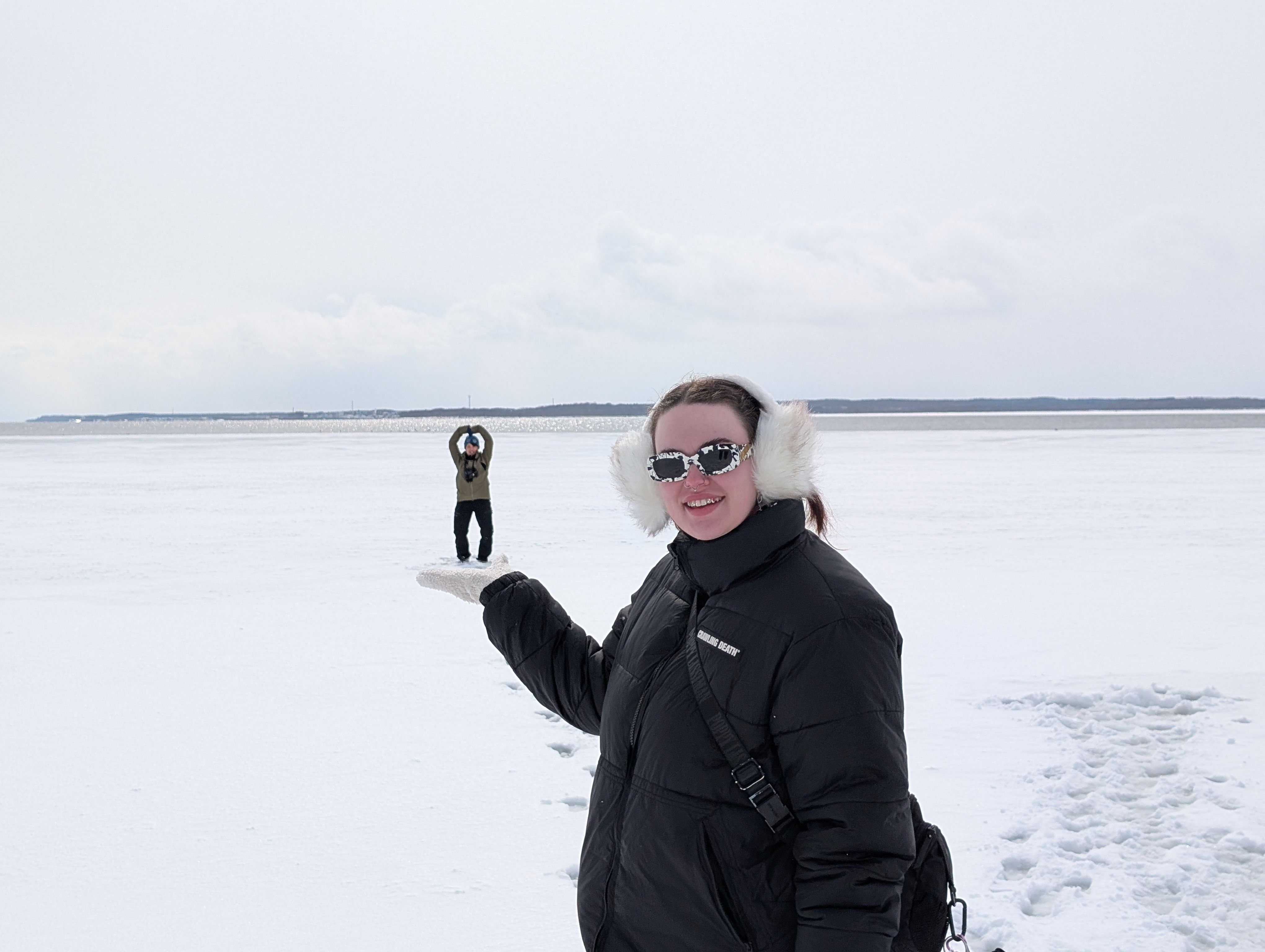 A woman holds her hand out in front of a large ice field while another woman further away poses. The photo creates an illusion such that the woman in the foreground looks as though she is holding a tiny person in the palm of her hand.