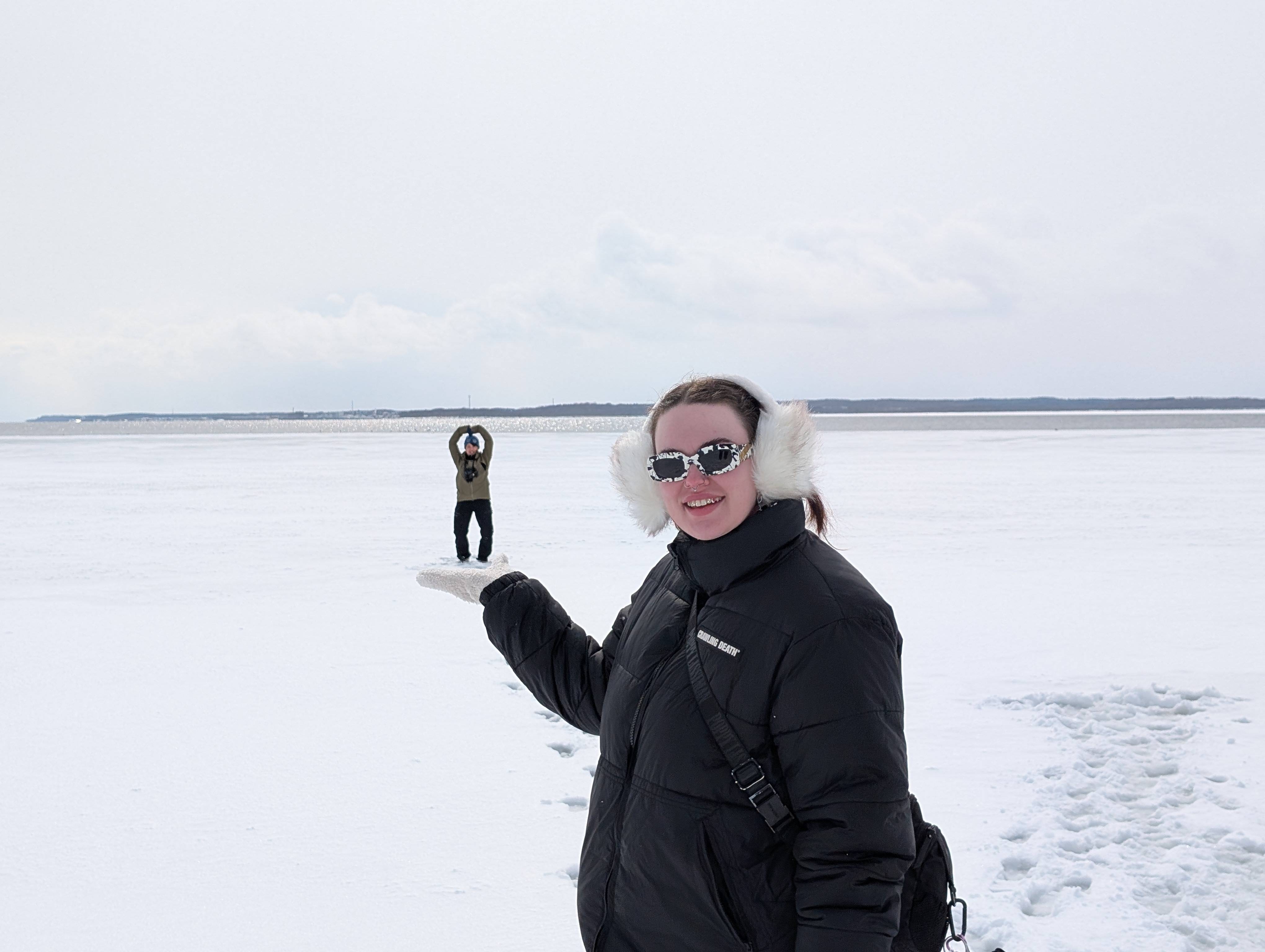 A woman holds her hand out in front of a large ice field while another woman further away poses. The photo creates an illusion such that the woman in the foreground looks as though she is holding a tiny person in the palm of her hand.