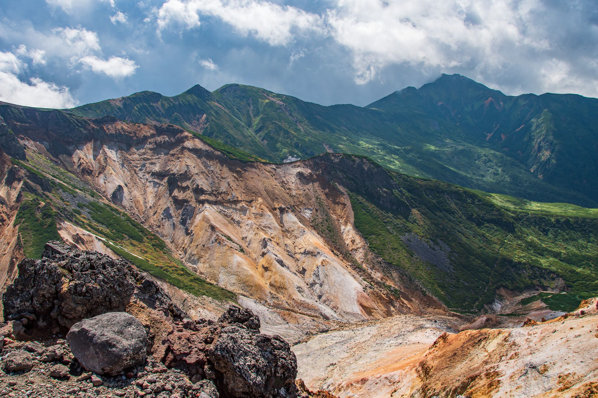 View of a volcanic crater from the summit of Mt. Sandan, the sand visibly different to the surrounding trees on the mountainside.