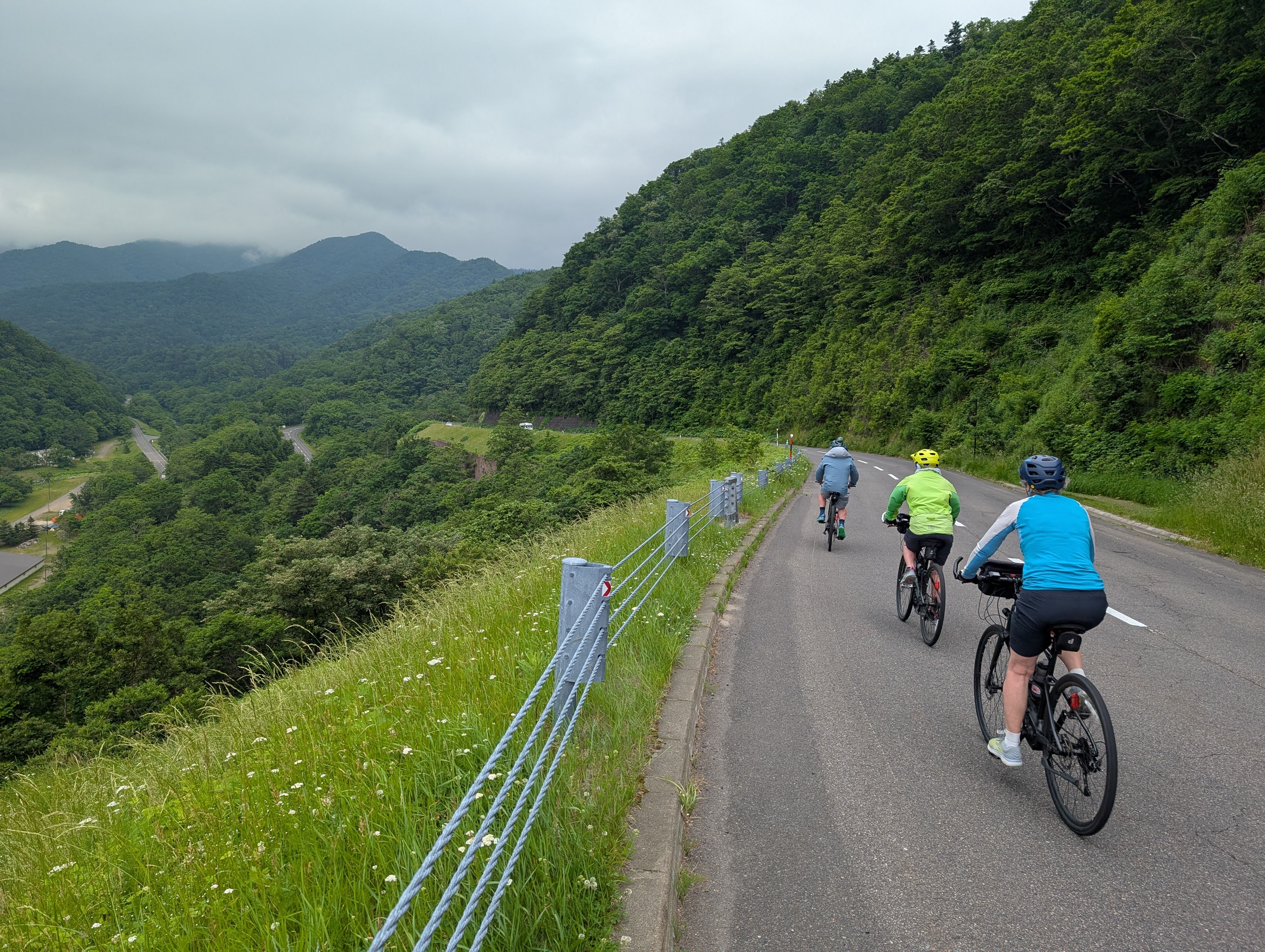 Three cyclists descend the Shiretoko Pass on a cloudy day.