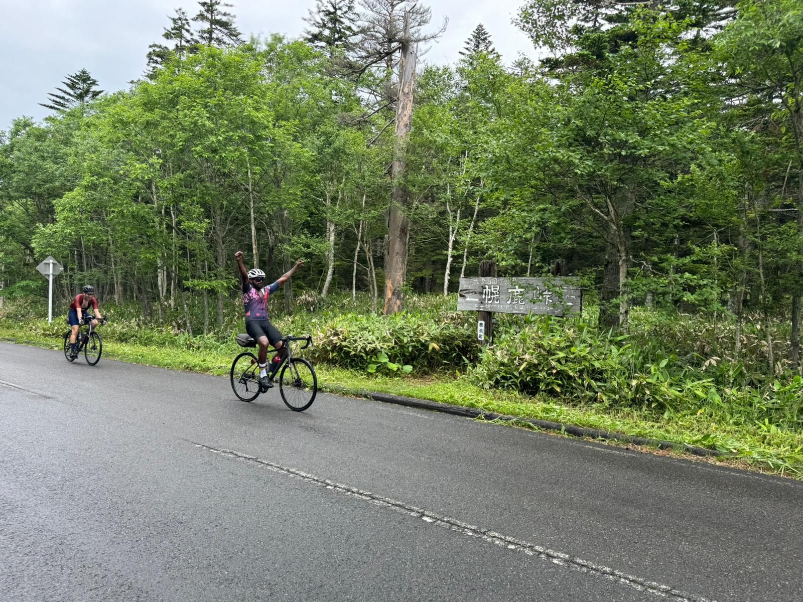 Two cyclists descend the Horoka Pass. One of them has their hands up in victory.