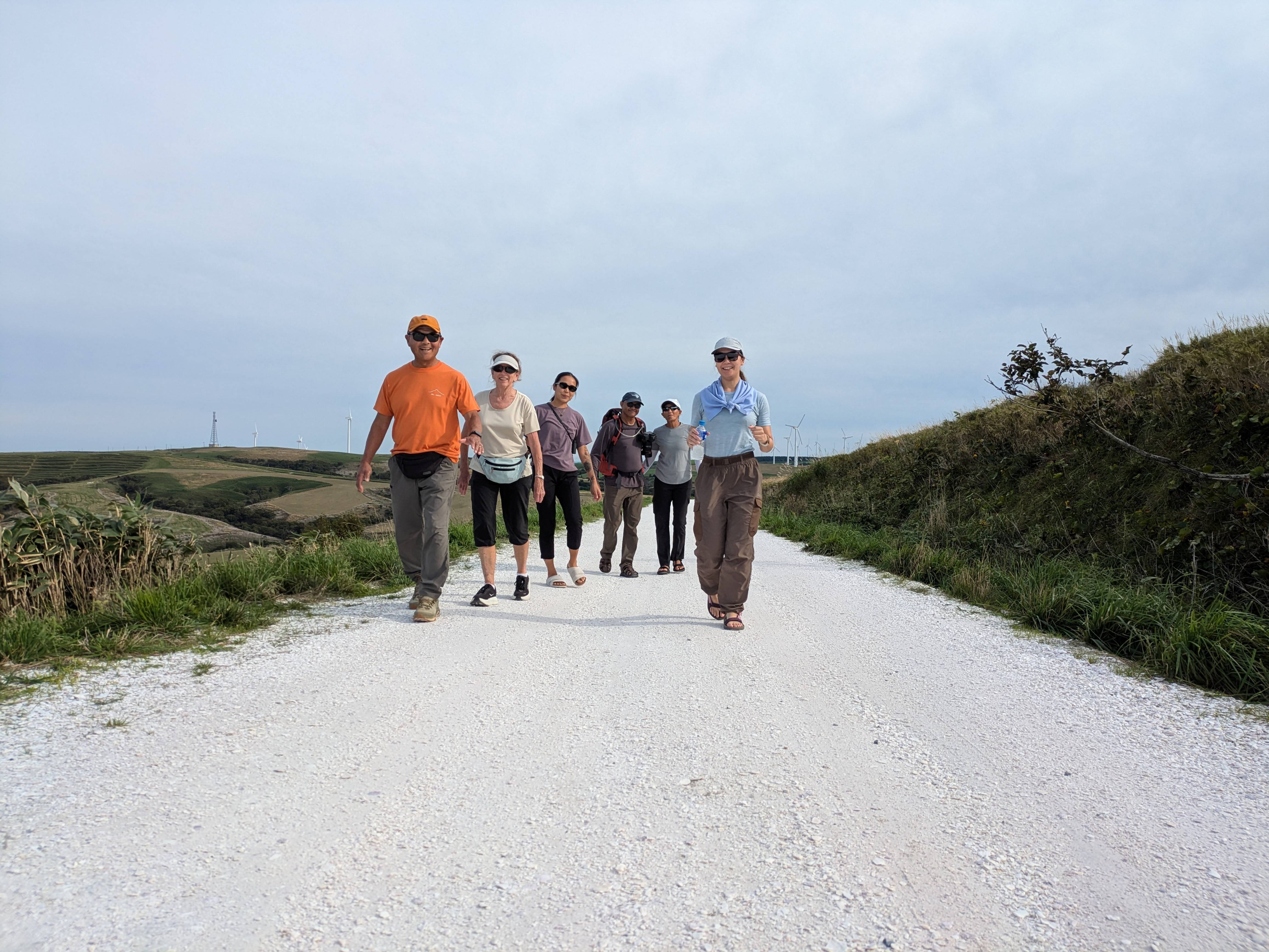 A group of walkers walk along the White Shell Path in Cape Soya, Hokkaido, smiling at the camera.