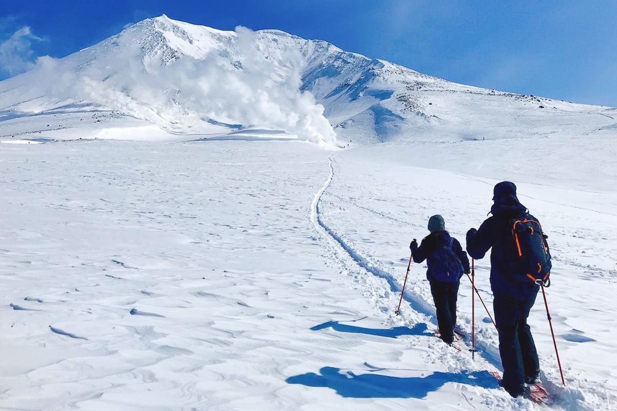 Two snowshoers make their way towards smoking fumaroles at the summit of Mt. Asahidake.