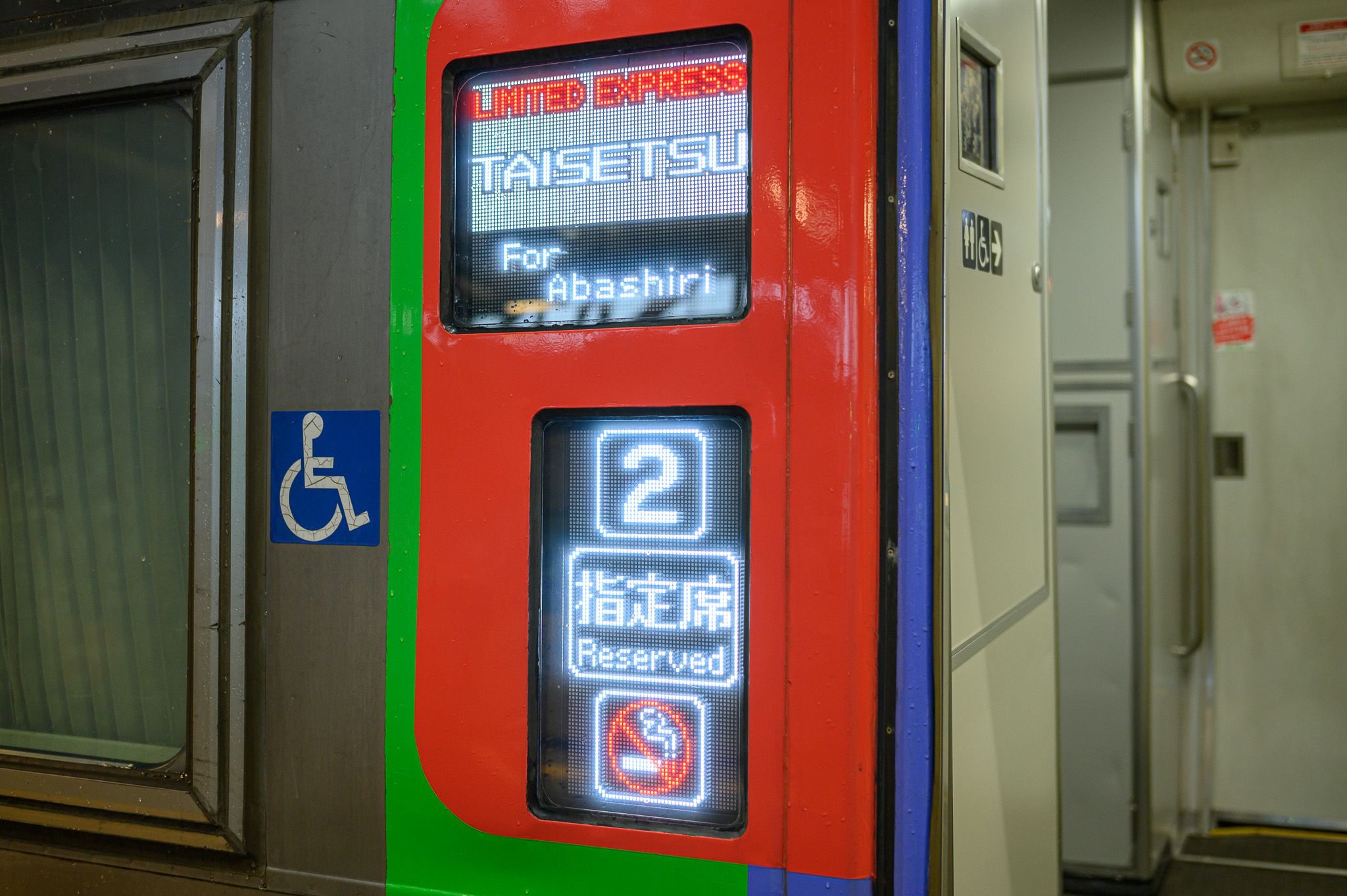 An electric billboard on the side of a limited express train. It states that the train is "Limited Express Taisetsu" bound for Abashiri. It indicates that the carriage is number 2, for reserved seat ticket holders only. A no-smoking symbol indicates it is a non-smoking train.
