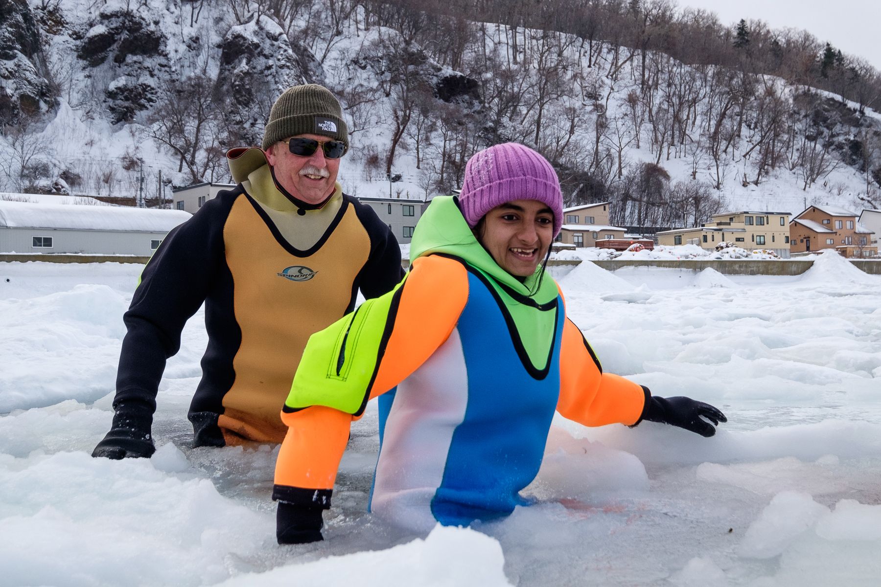 Two tourists wearing dry suites wade through the Sea of Okhotsk surrounded by drift ice.